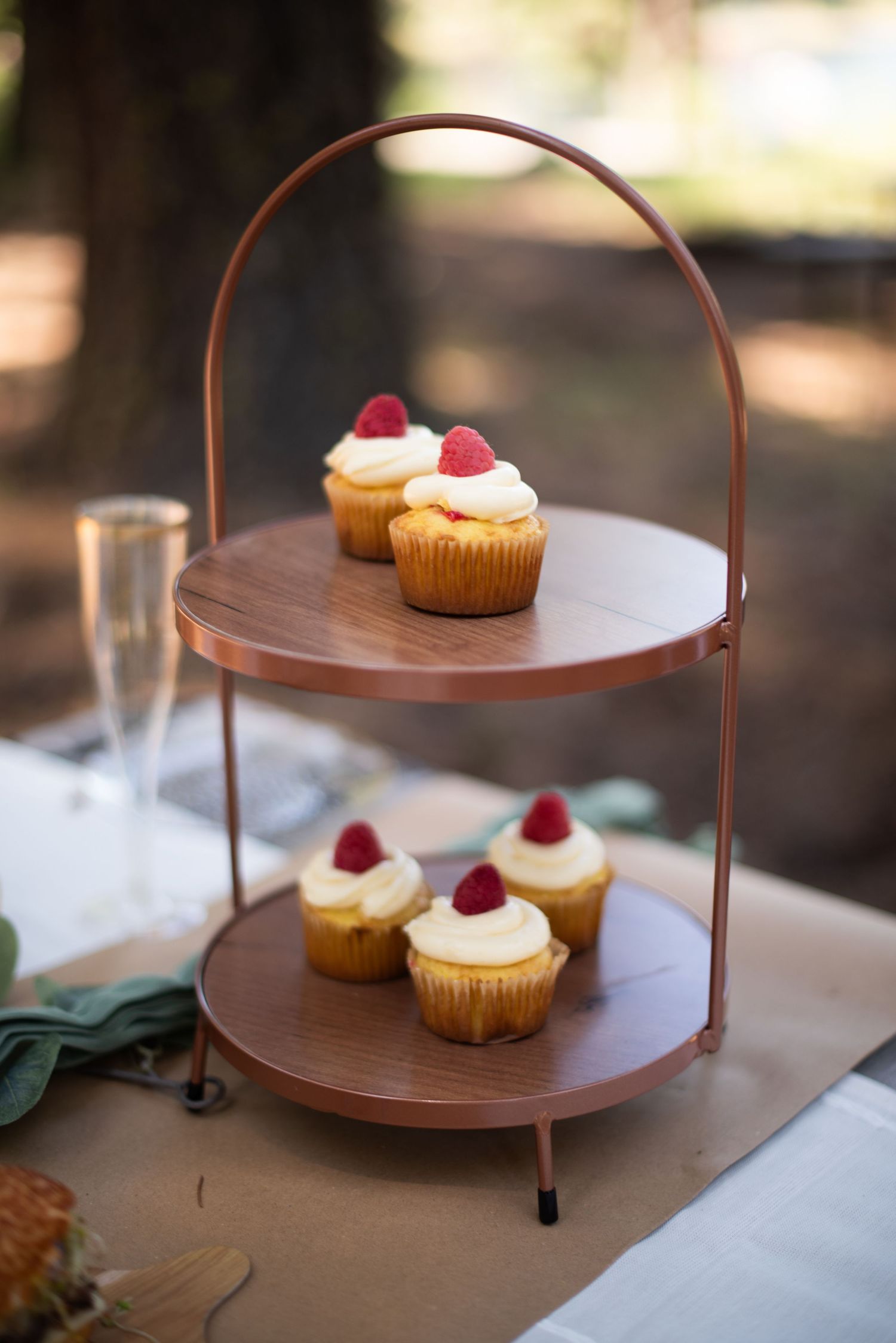 Two-tier copper cupcake stand with vanilla frosted cupcakes topped with raspberries at a wedding.
