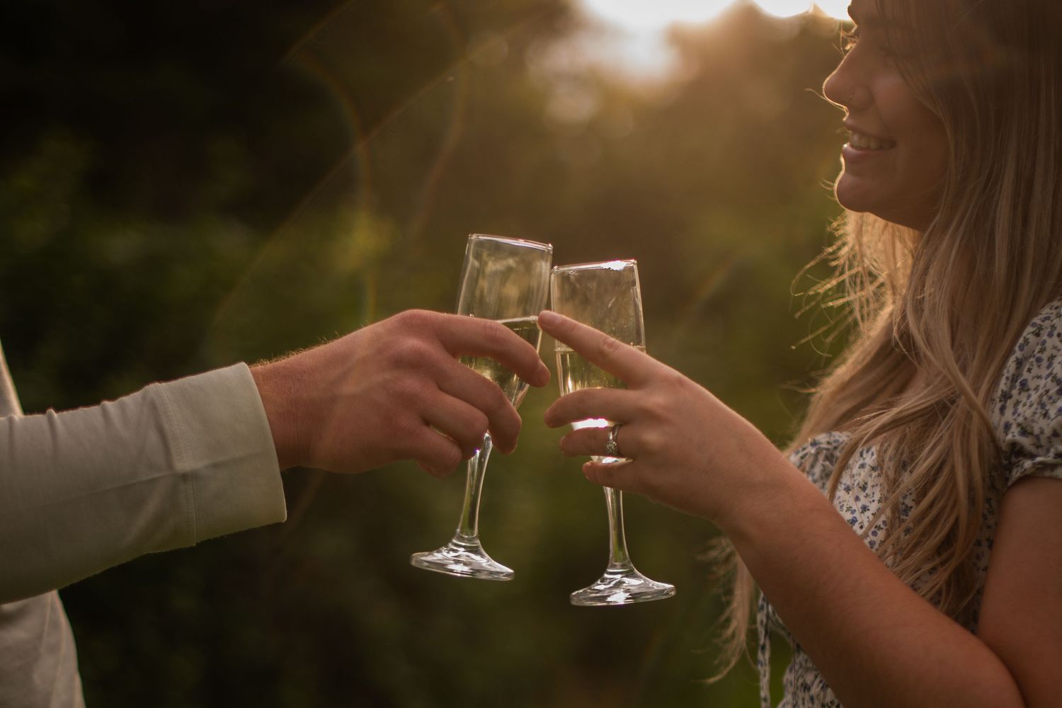 Couple clinking champagne glasses together outdoors at golden hour in a lush green garden setting.