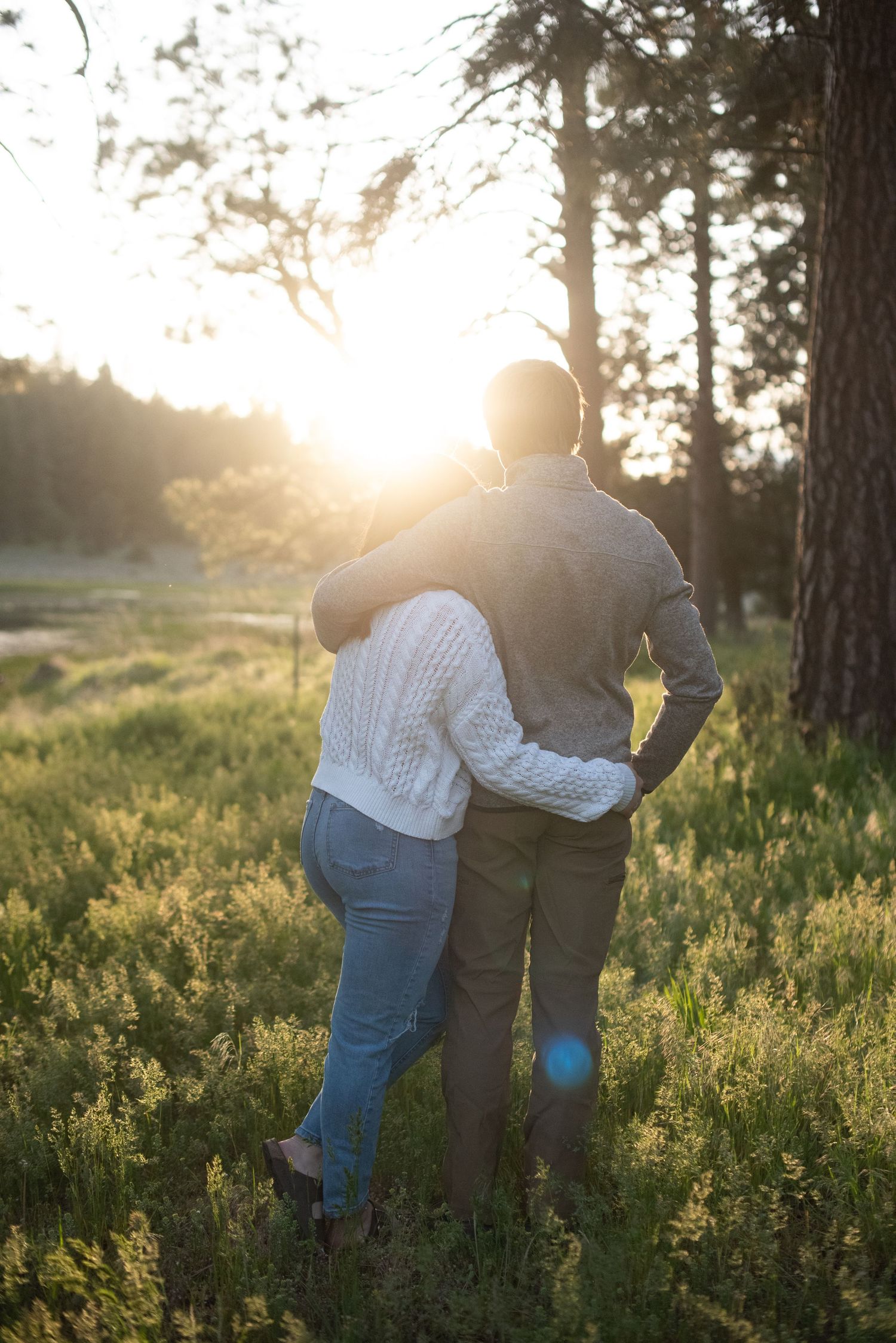 Couple embracing while watching a golden sunset in a forest meadow.