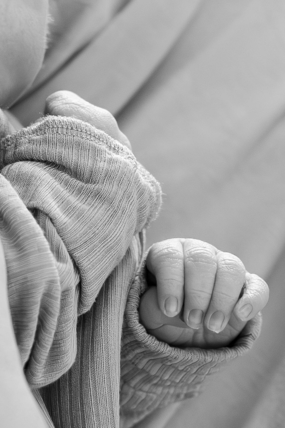 Black and white close-up of a newborn baby's tiny hand grasping fabric.