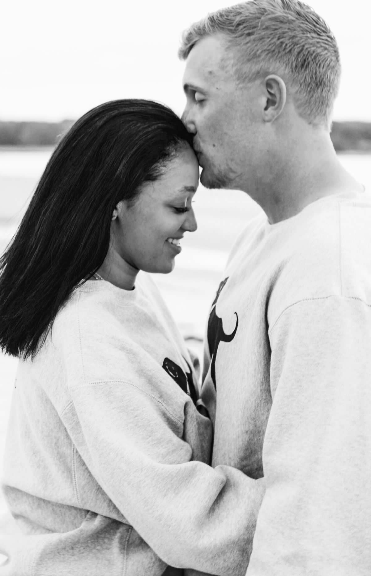 A black and white photo of a couple sharing an intimate moment in matching sweatshirts.