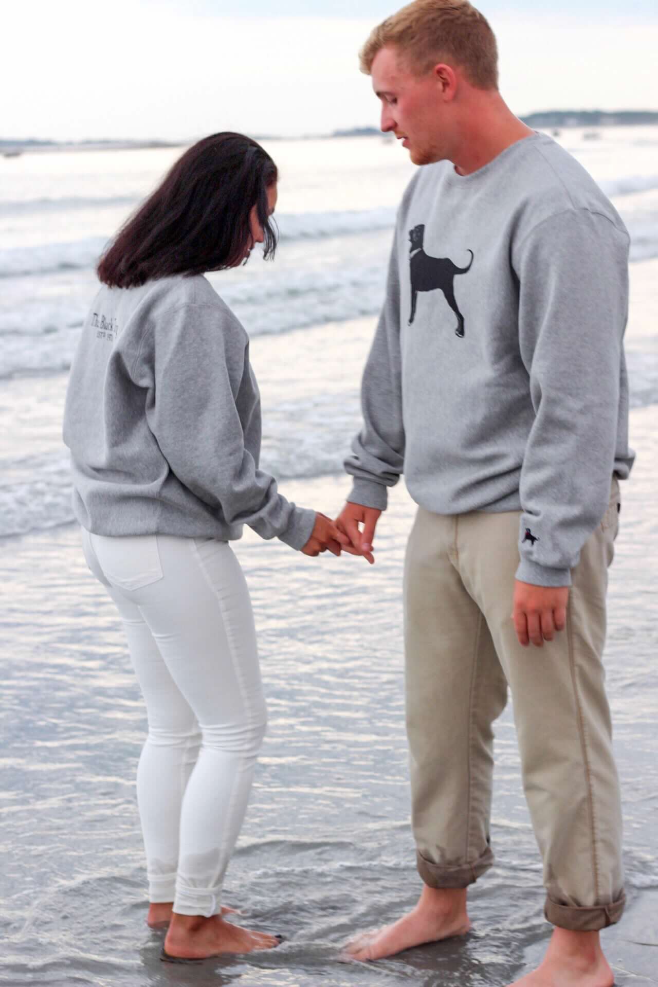 Couple in coordinated outfits walking barefoot in shallow beach water.
