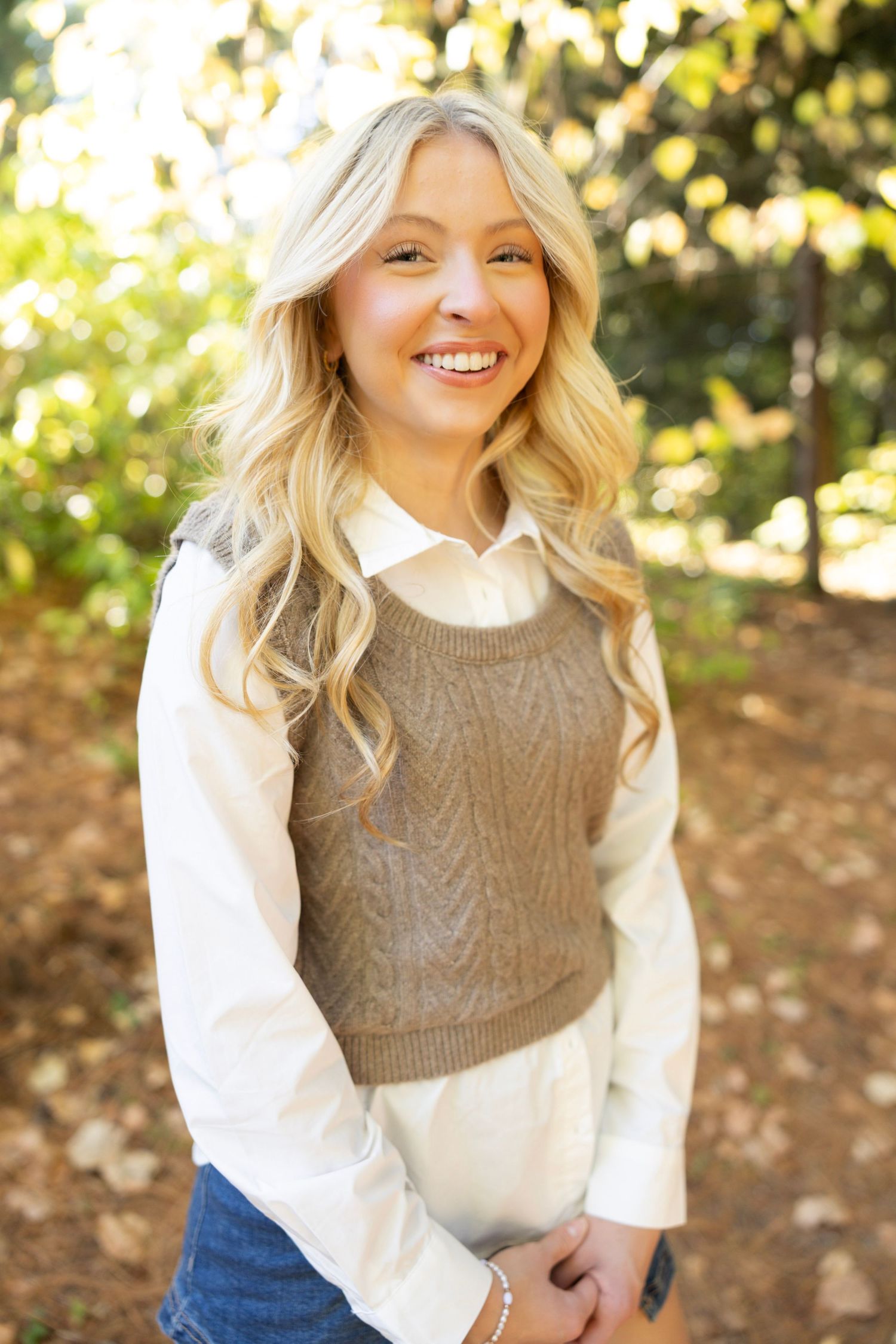 Natural outdoor portrait showcasing fall layers with tan sweater vest against autumn foliage.