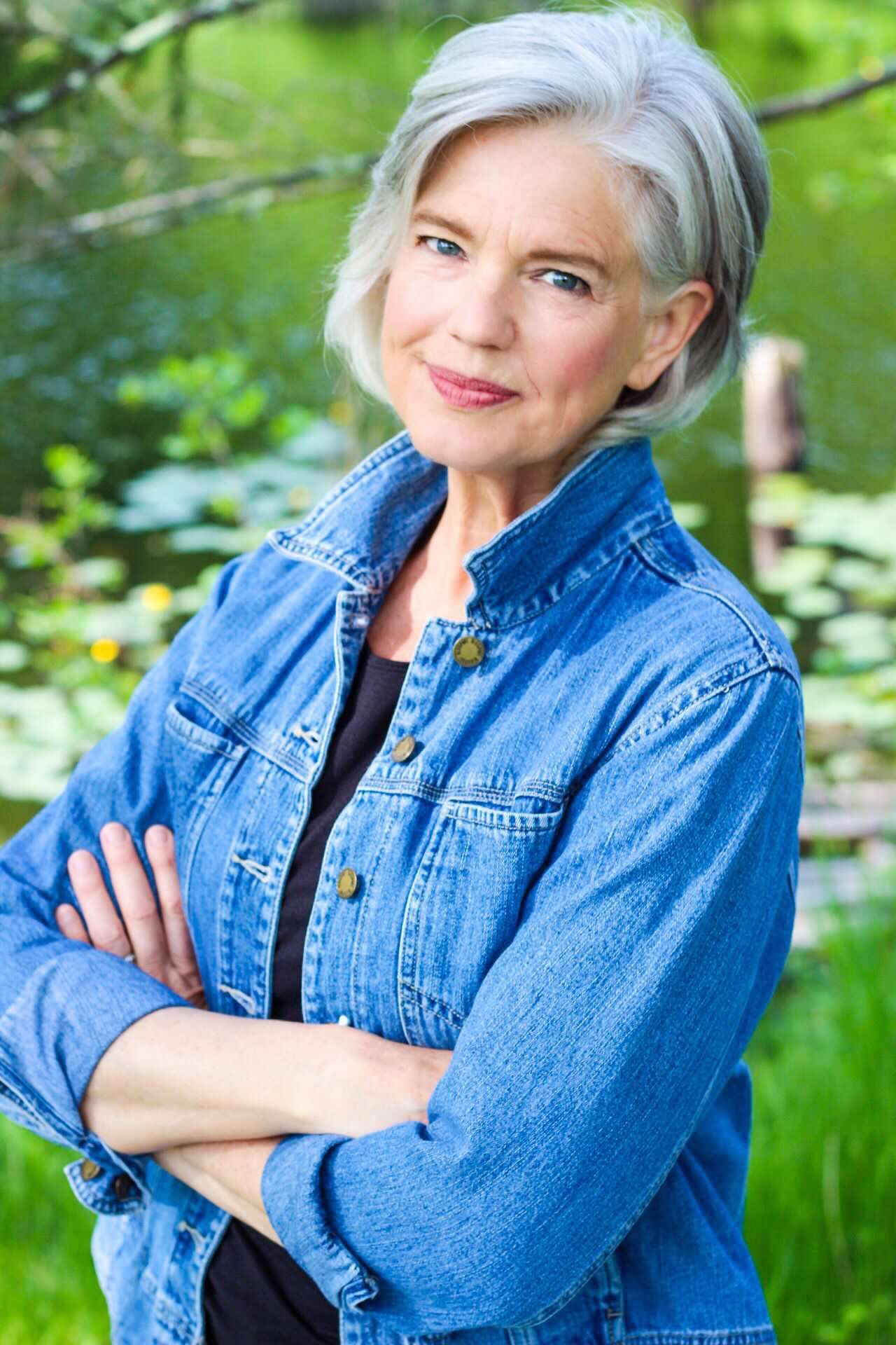 Person in denim jacket poses outdoors against green natural background.