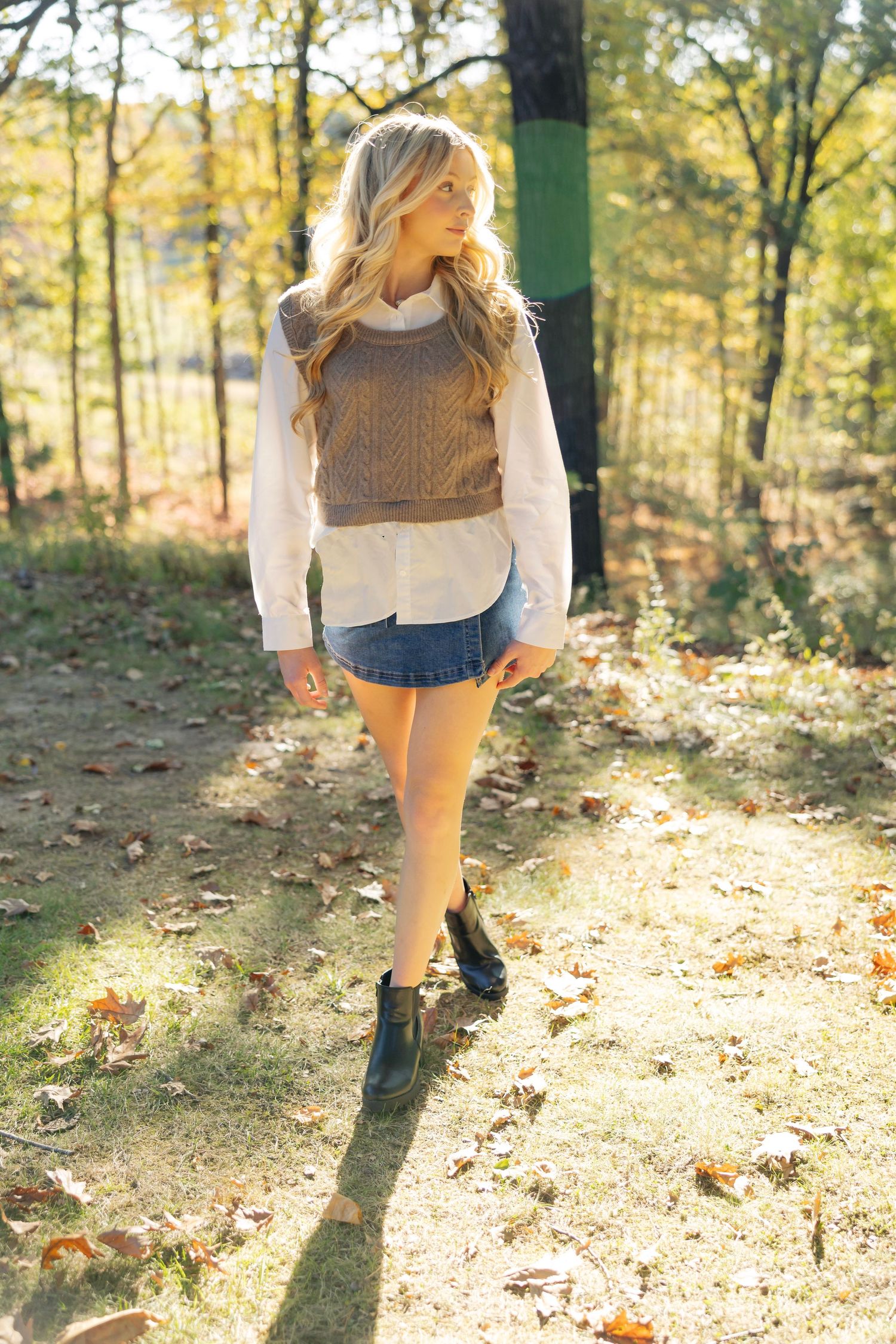 Casual fall outfit with sweater vest and denim photographed in a sunlit wooded setting.