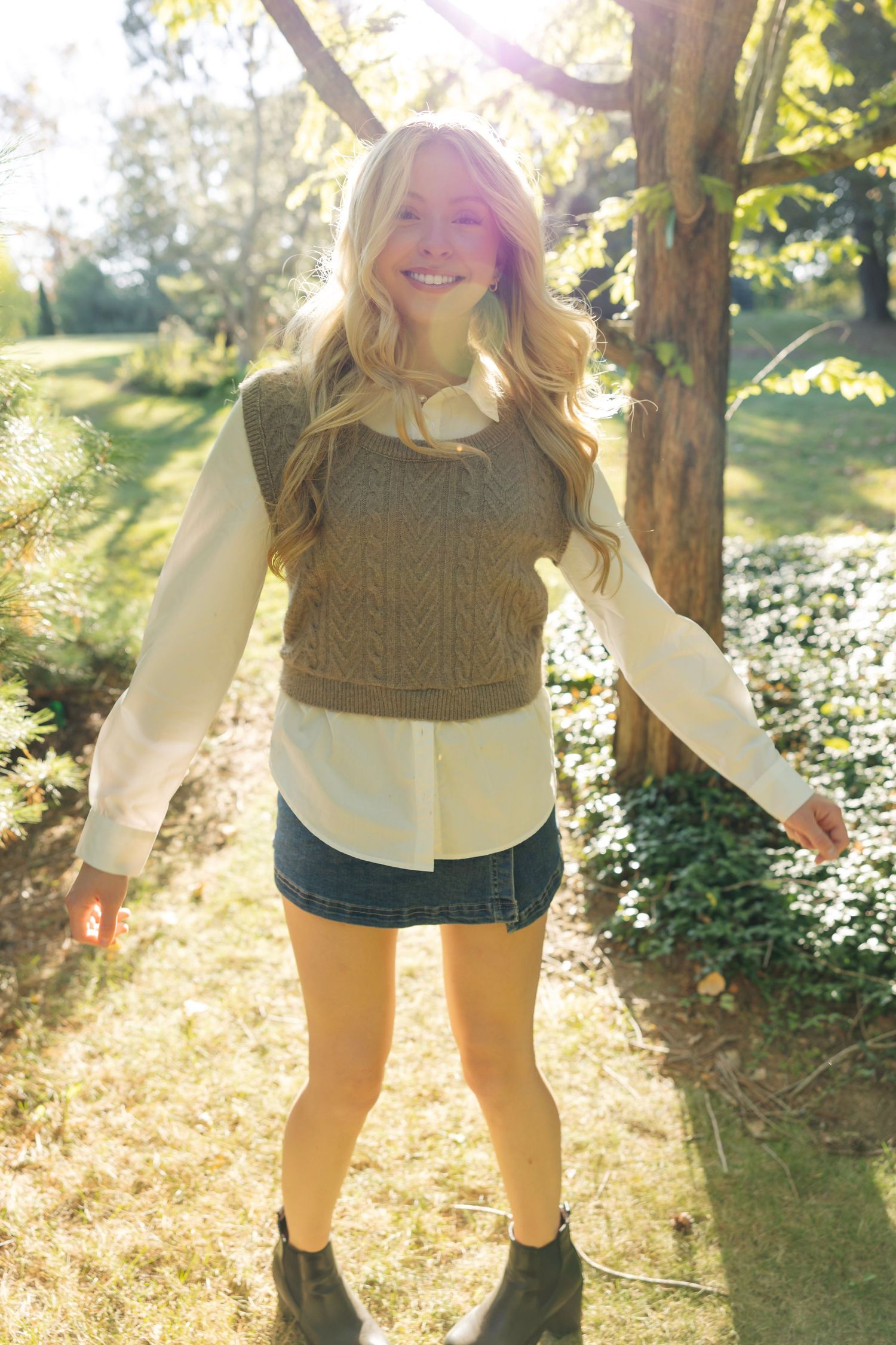 A cozy autumn outfit with a brown knit sweater and white blouse photographed in dappled sunlight.