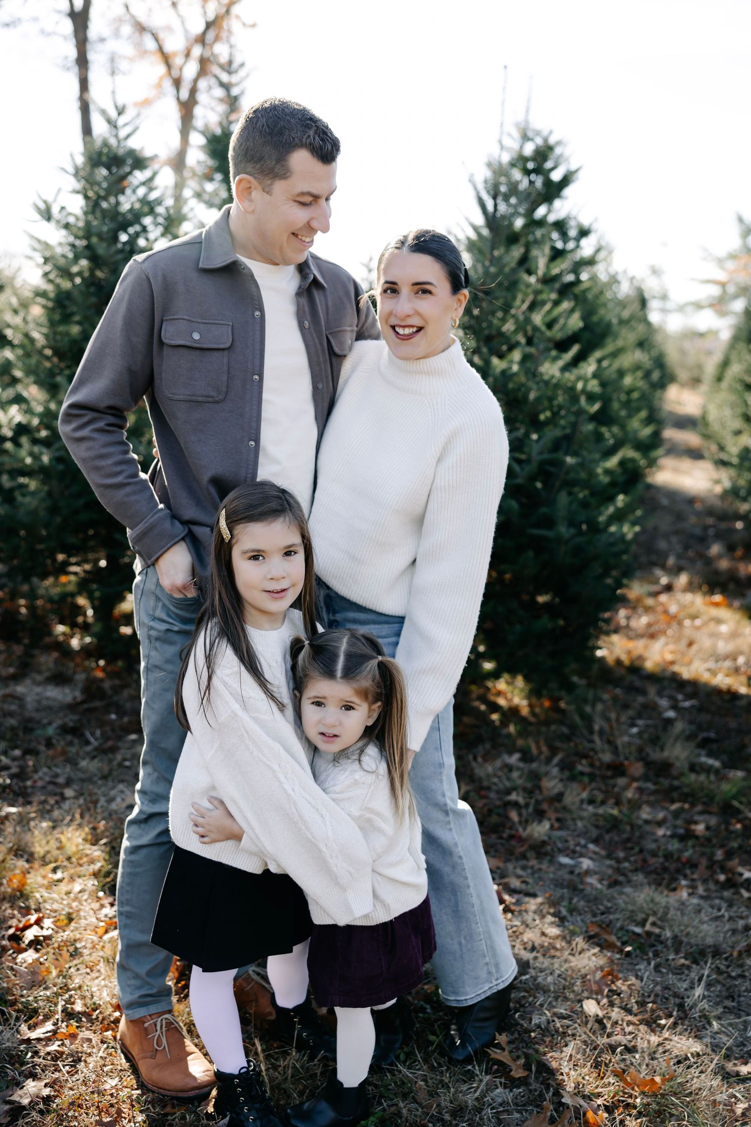 A loving family shares tender moments together while posing outdoors near evergreen trees.
