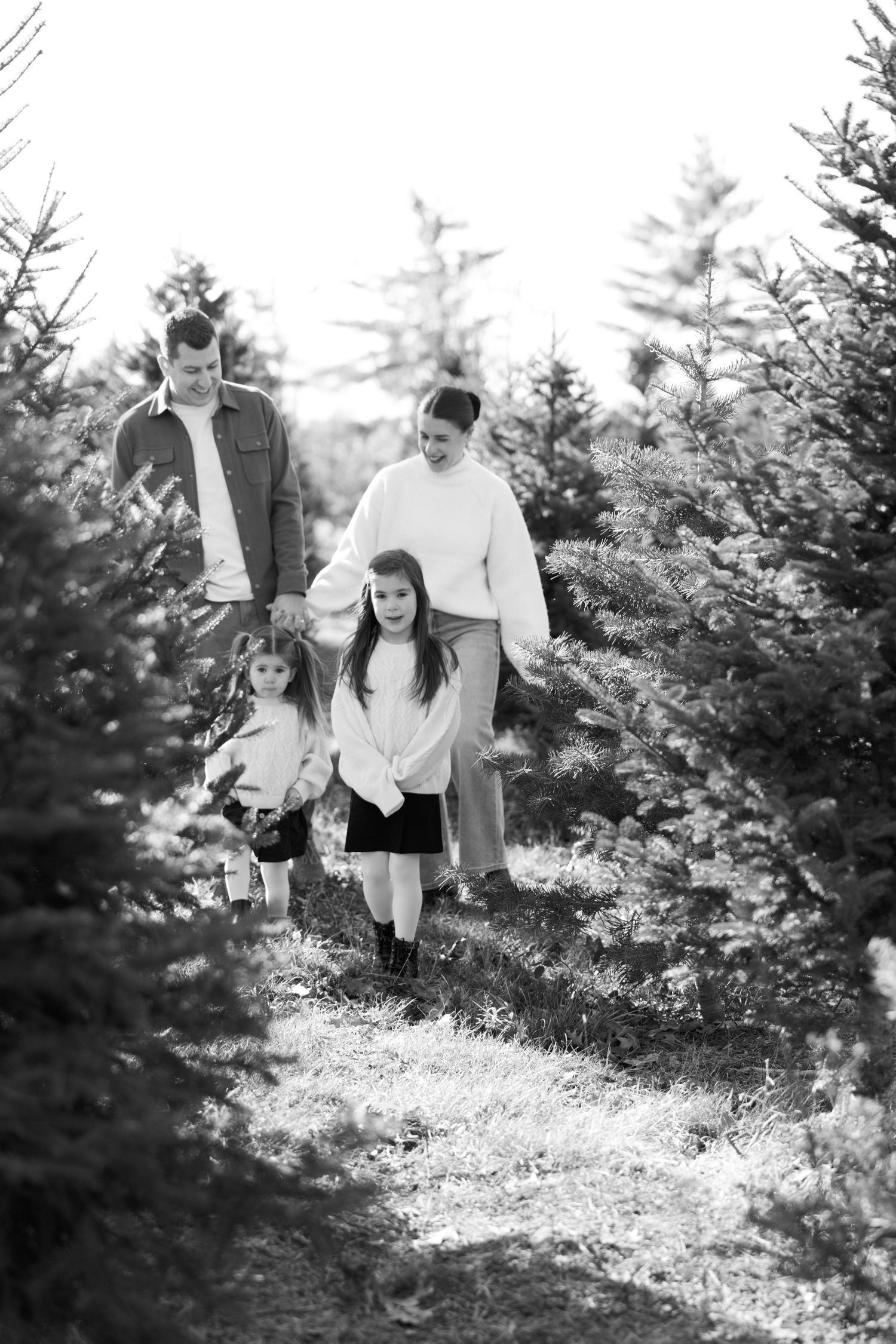 A black and white photo captures a family's playful moments among pine trees.