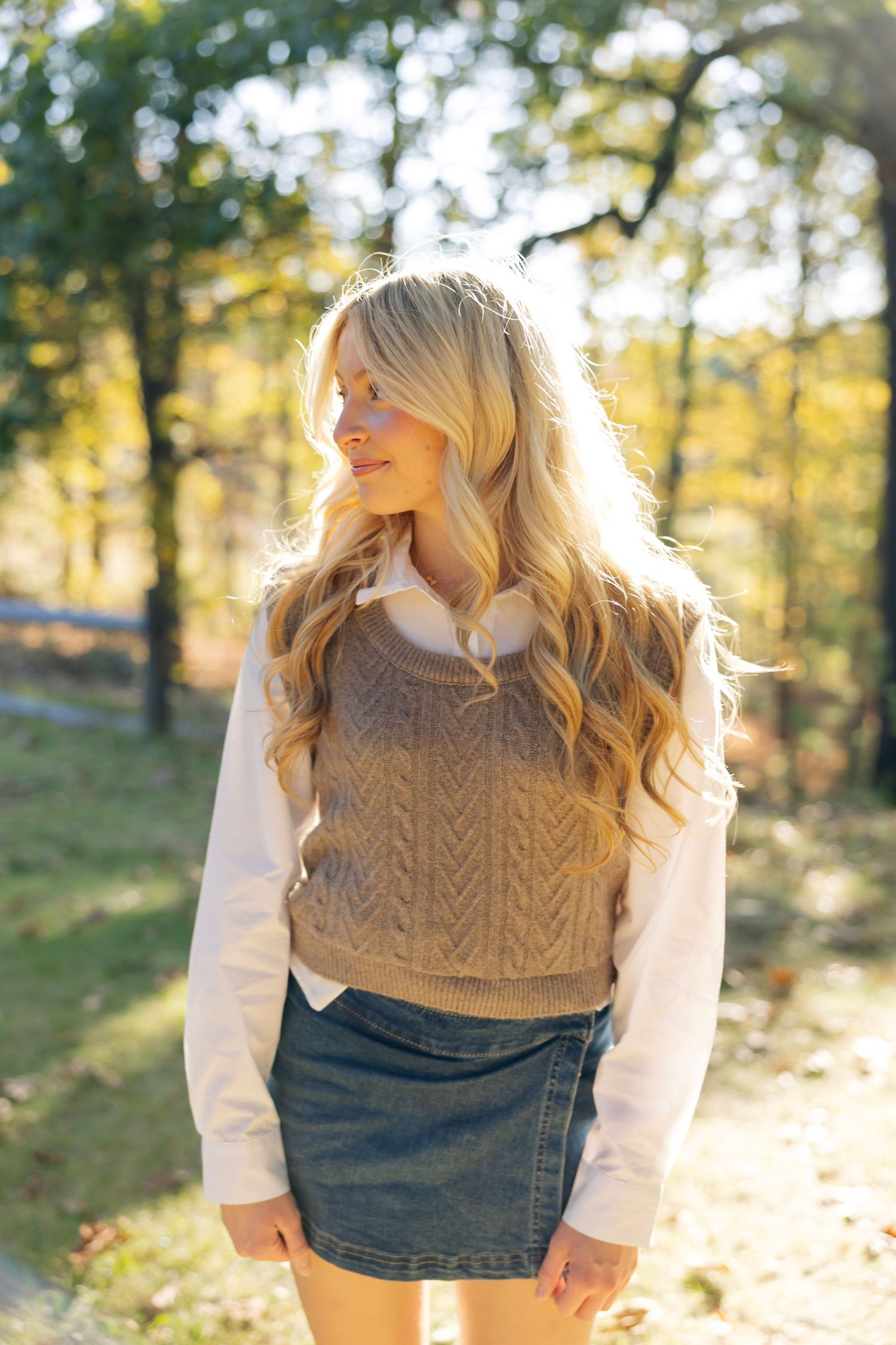 Autumn fashion photo with tan cable knit vest and white shirt against golden sunlit trees.