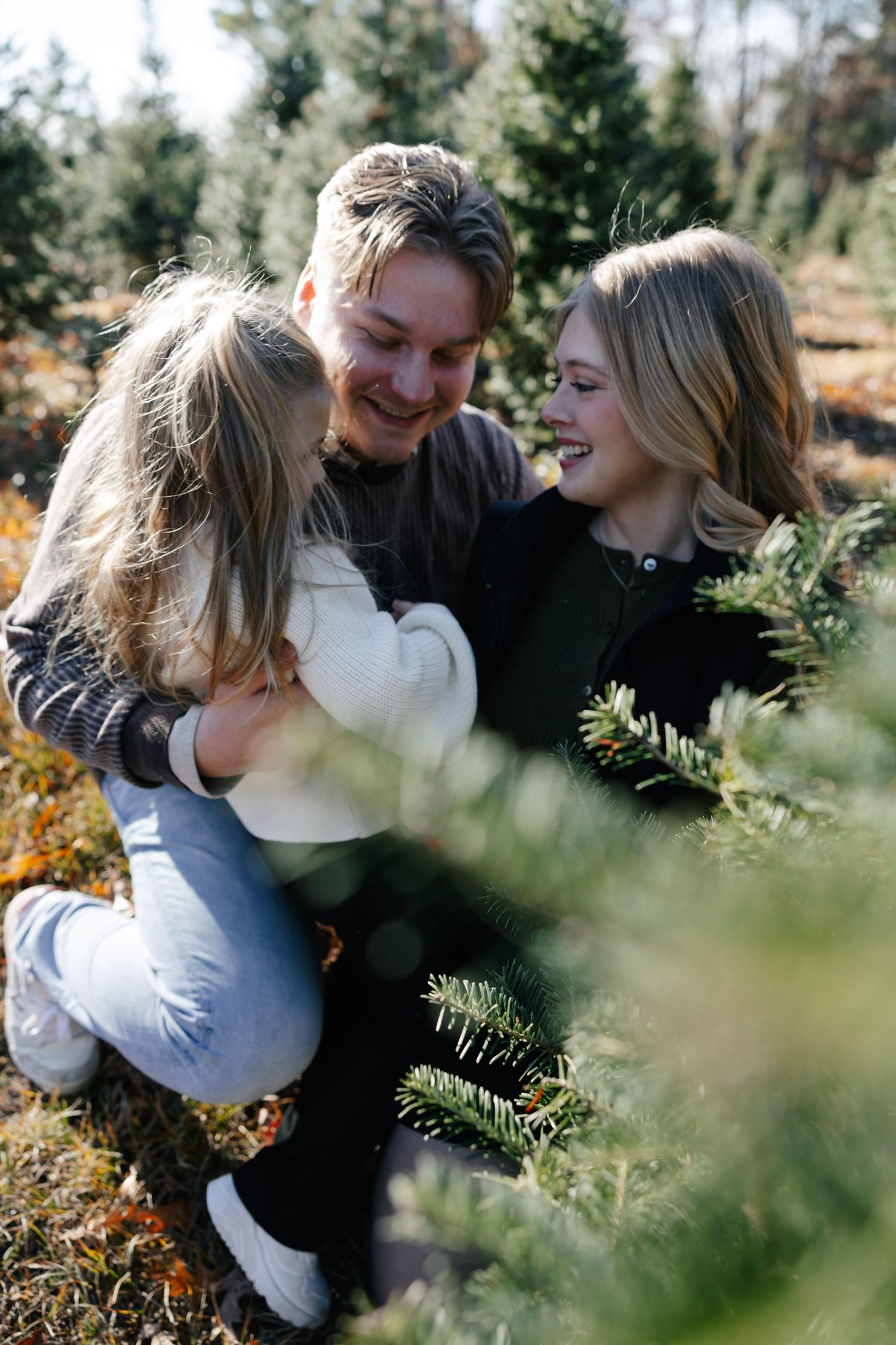 Playful couple embracing outdoors in a natural setting with evergreen trees in the background.