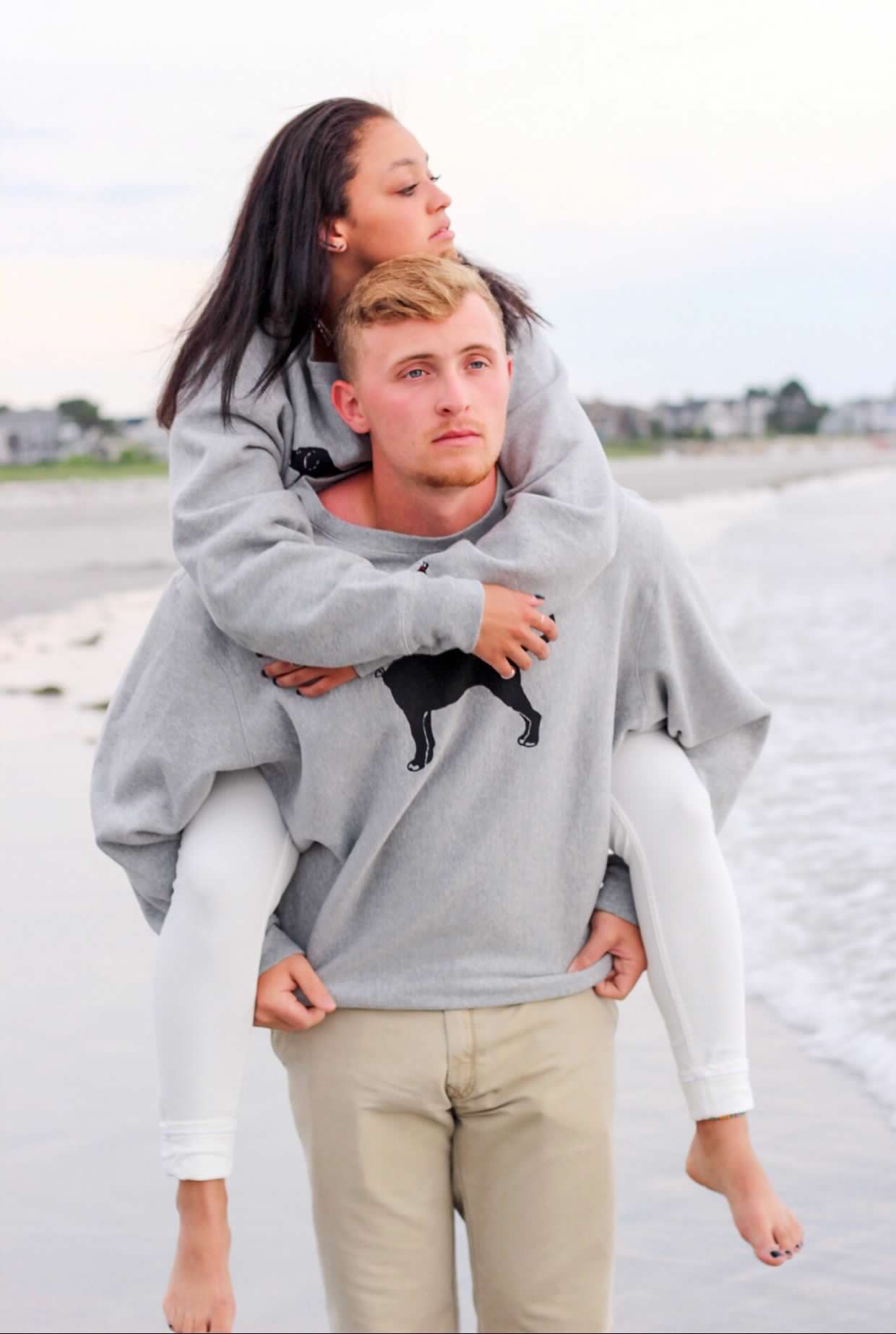 Couple in grey sweatshirts sharing playful moment on sandy beach.