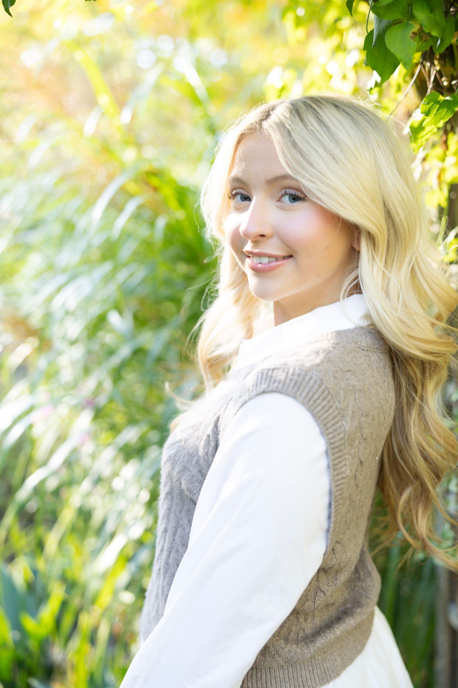 Sun-drenched outdoor portrait featuring classic fall layers and natural garden backdrop.