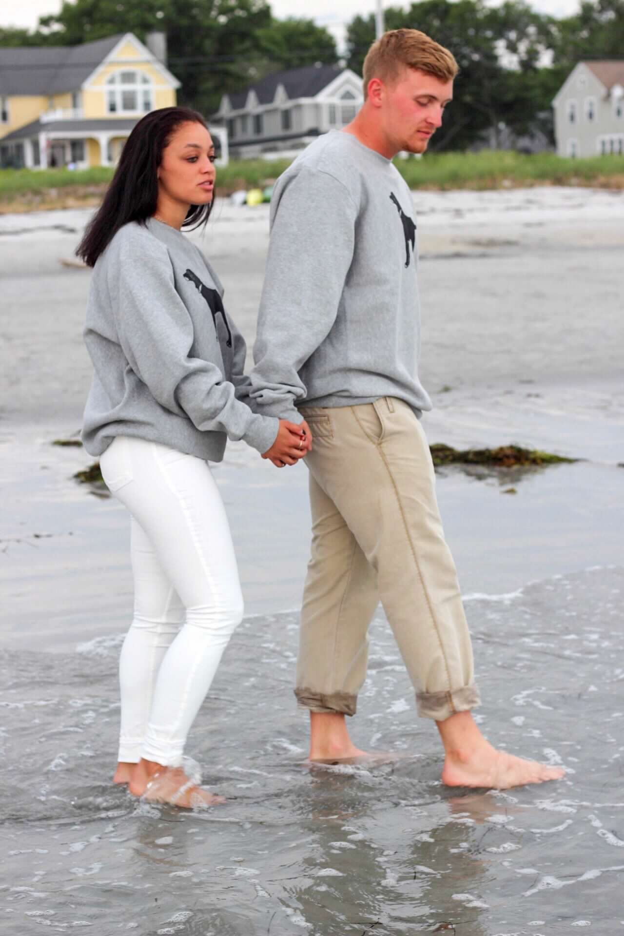 Couple splashing and playing in ankle-deep ocean water at the beach.