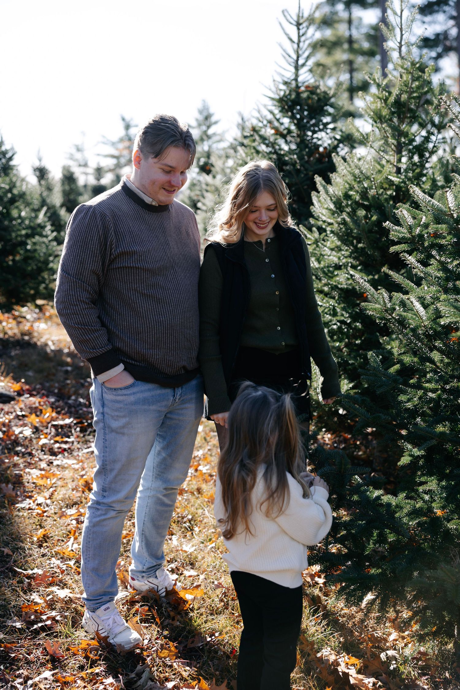 Family walking together through rows of Christmas trees on a sunny autumn afternoon.