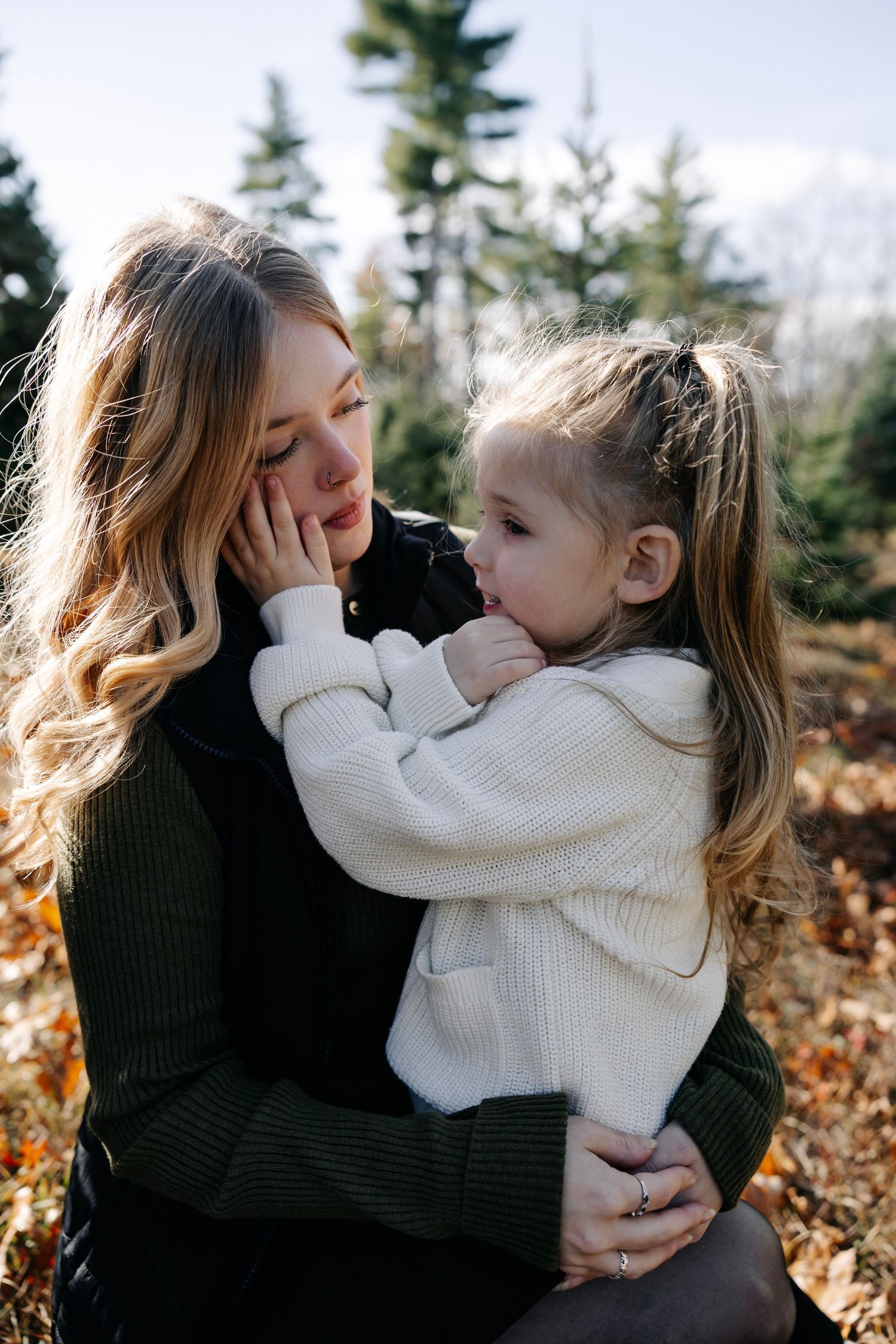 Tender family moment captured outdoors among pine trees on a bright day.