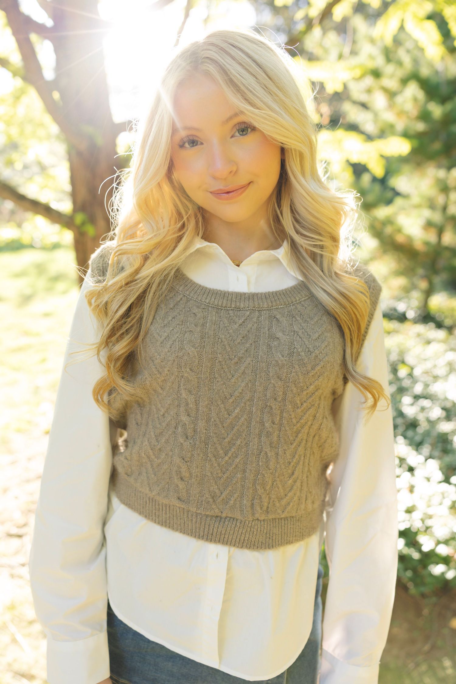 A fashionable layered look with a gray cable knit sweater over a white collared shirt.