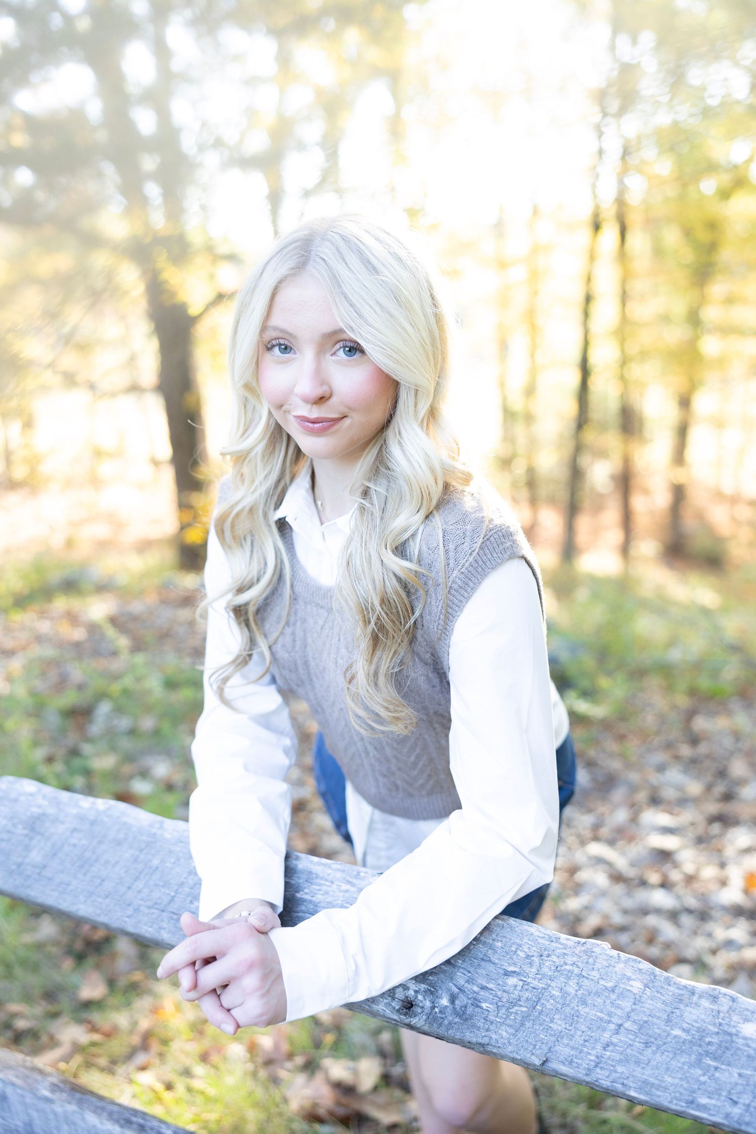 Outdoor portrait by wooden fence featuring layered autumn outfit with gray knit vest.