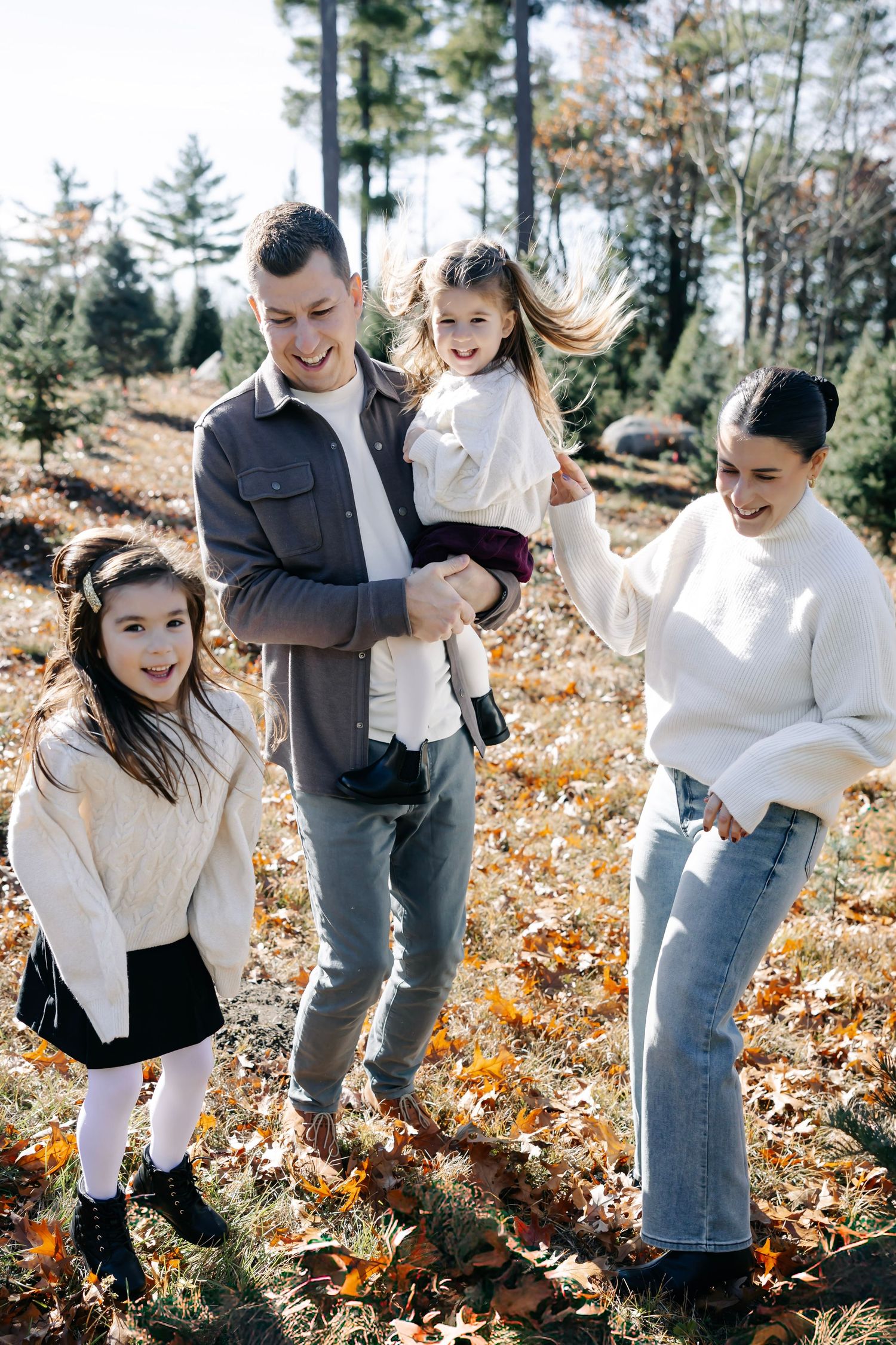 Family having fun and playing together on fallen autumn leaves among evergreen trees.