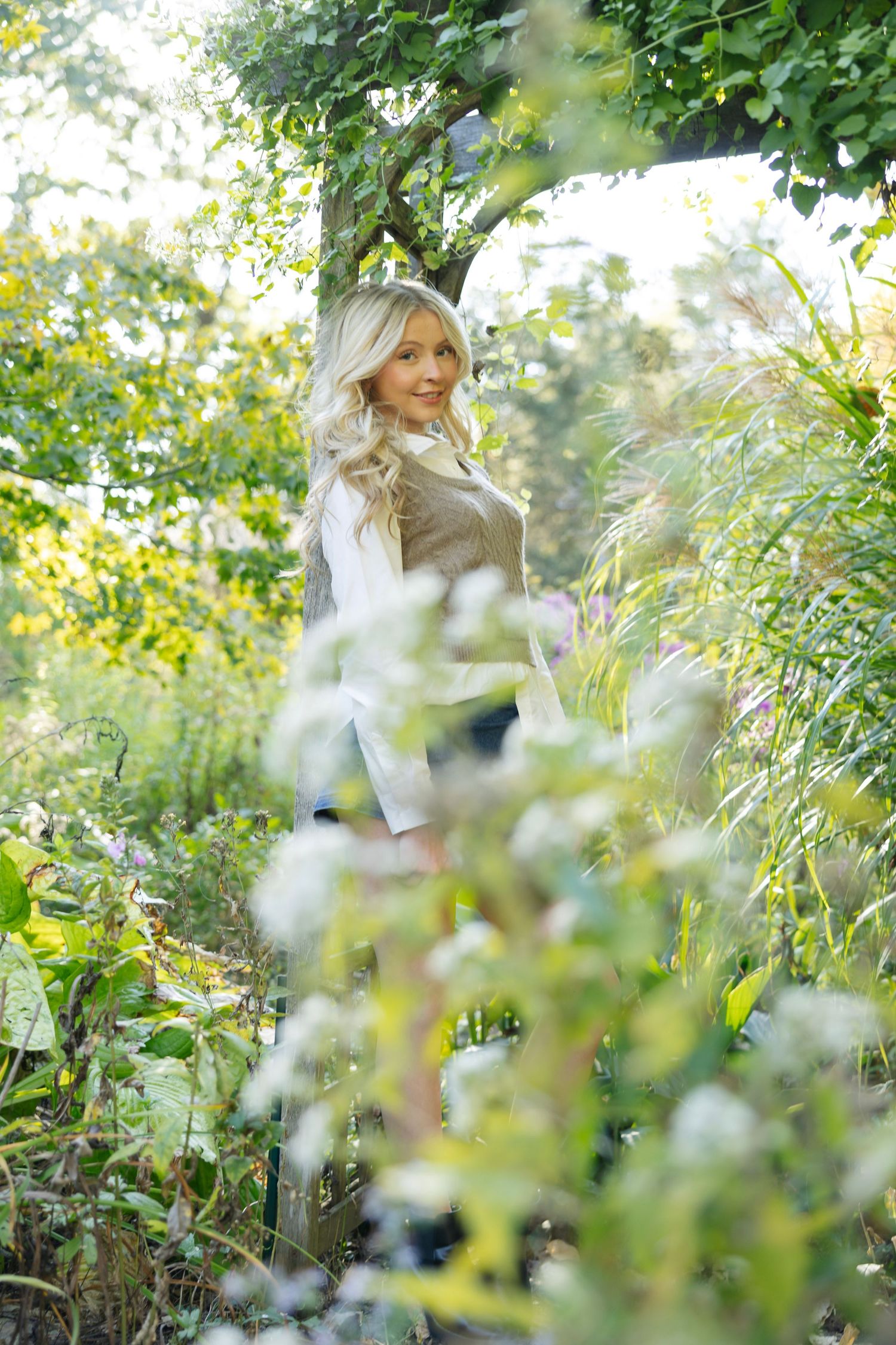 Ethereal garden portrait through foliage with soft lighting and classic fall layered outfit.