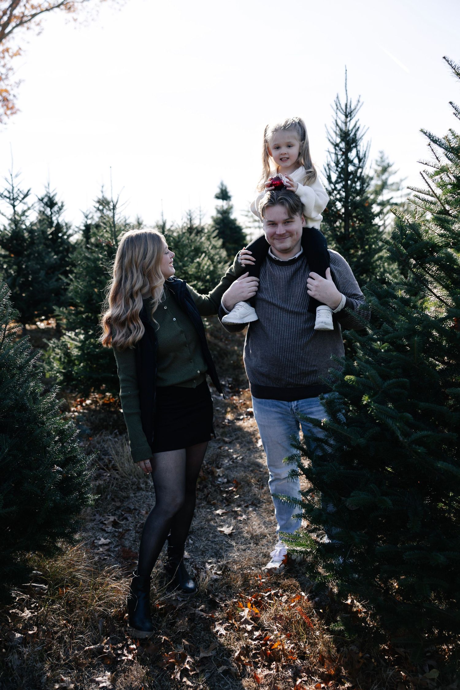Family walking together through evergreen trees at a Christmas tree farm on a sunny winter day.