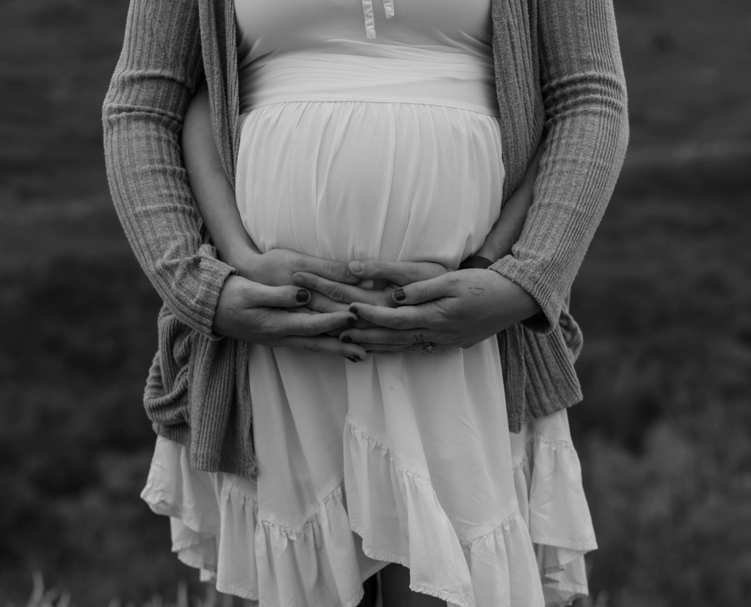a black and white closeup shot of a pregnant woman. she is holding her hands around her belly with a man's hands around hers.