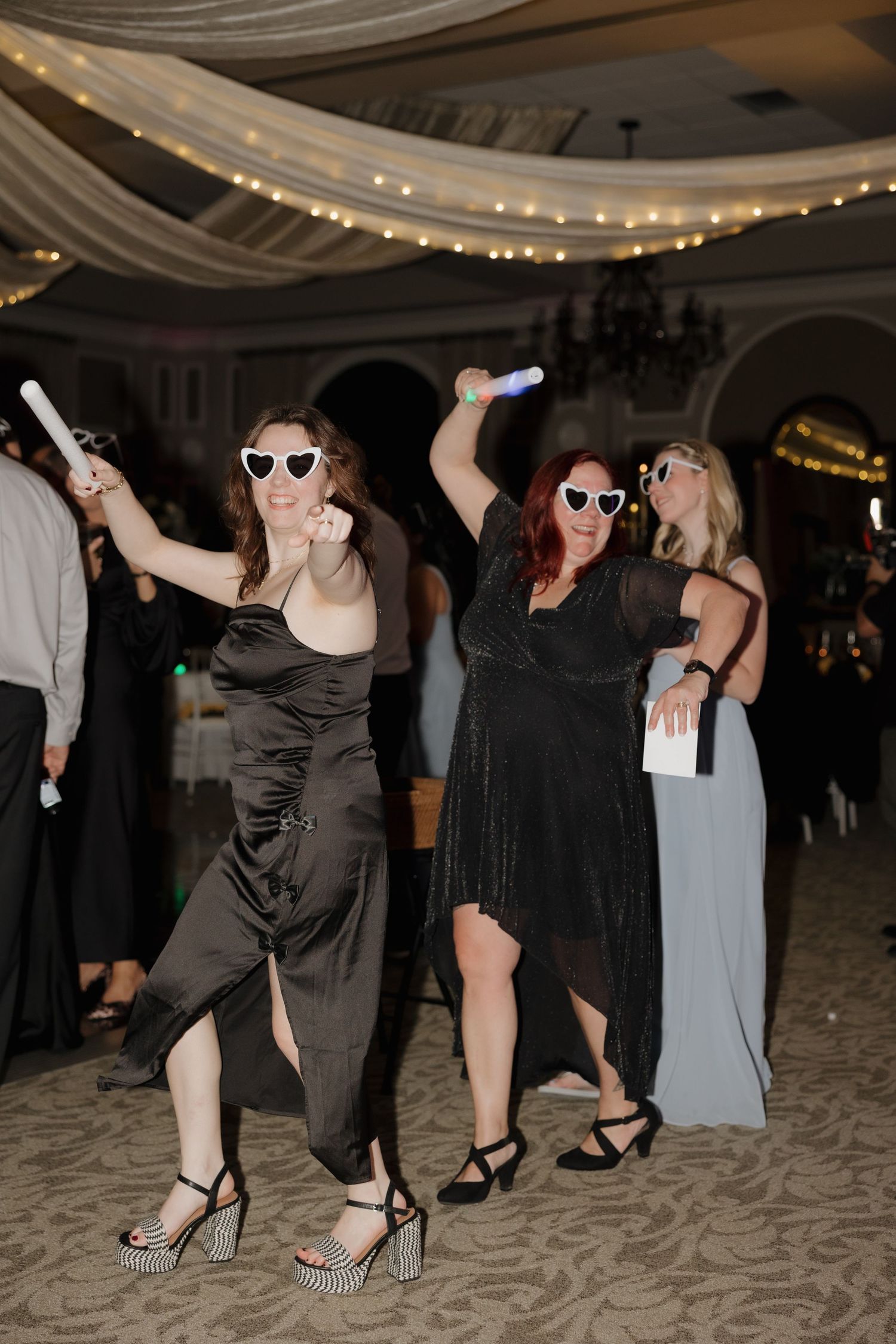 Wedding reception dance floor filled with guests dancing and having fun under string lights.