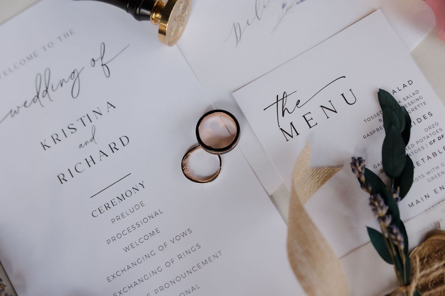 Wedding rings rest on elegant stationery featuring ceremony program and menu cards for Kristina and Richard's wedding.