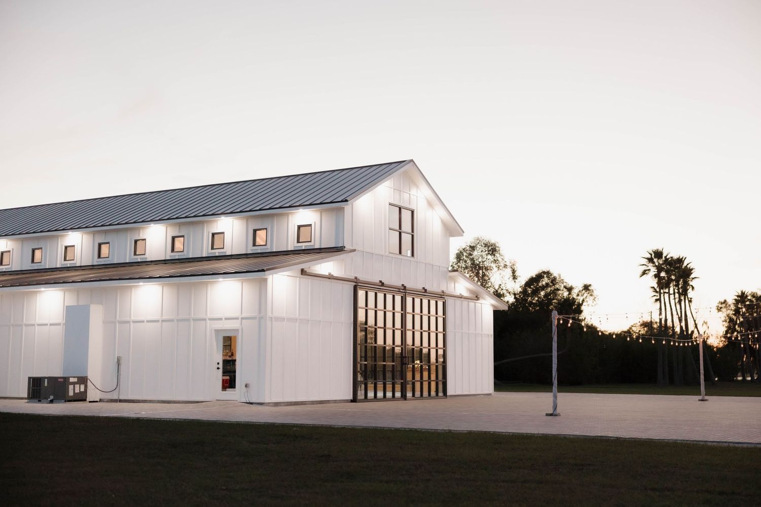 Modern white barn-style event venue with glass windows and exterior lighting at dusk.