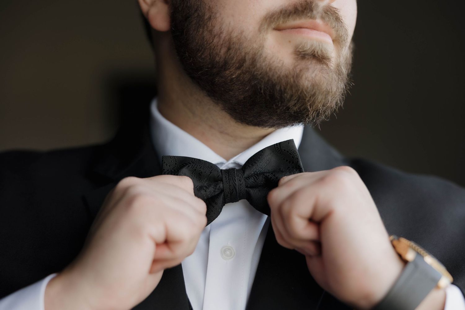 Close-up shots of a black bowtie being adjusted and tied on a formal tuxedo shirt collar.