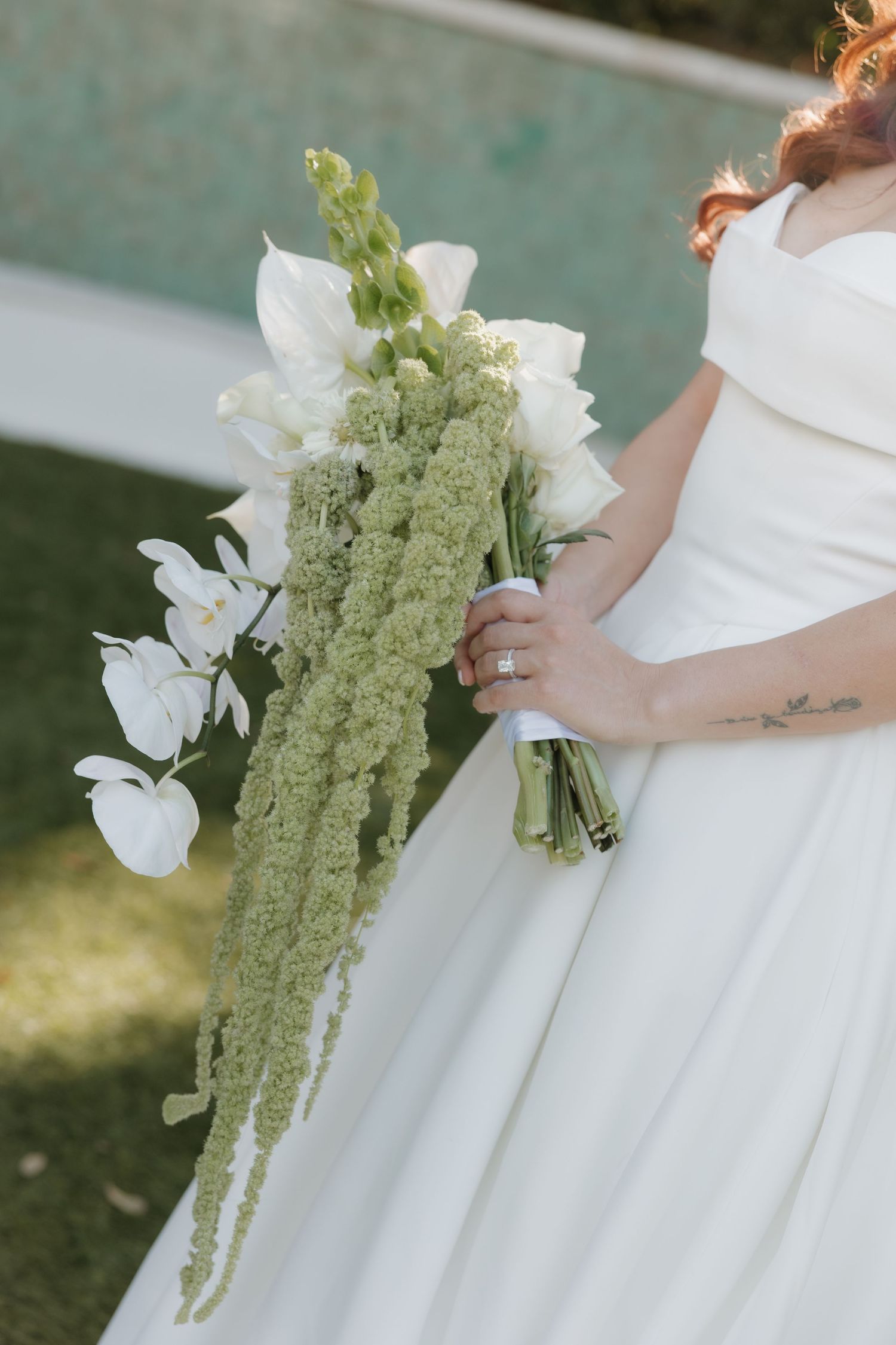 Elegant white wedding bouquet featuring cascading green amaranthus and white orchids held against a flowing white dress.