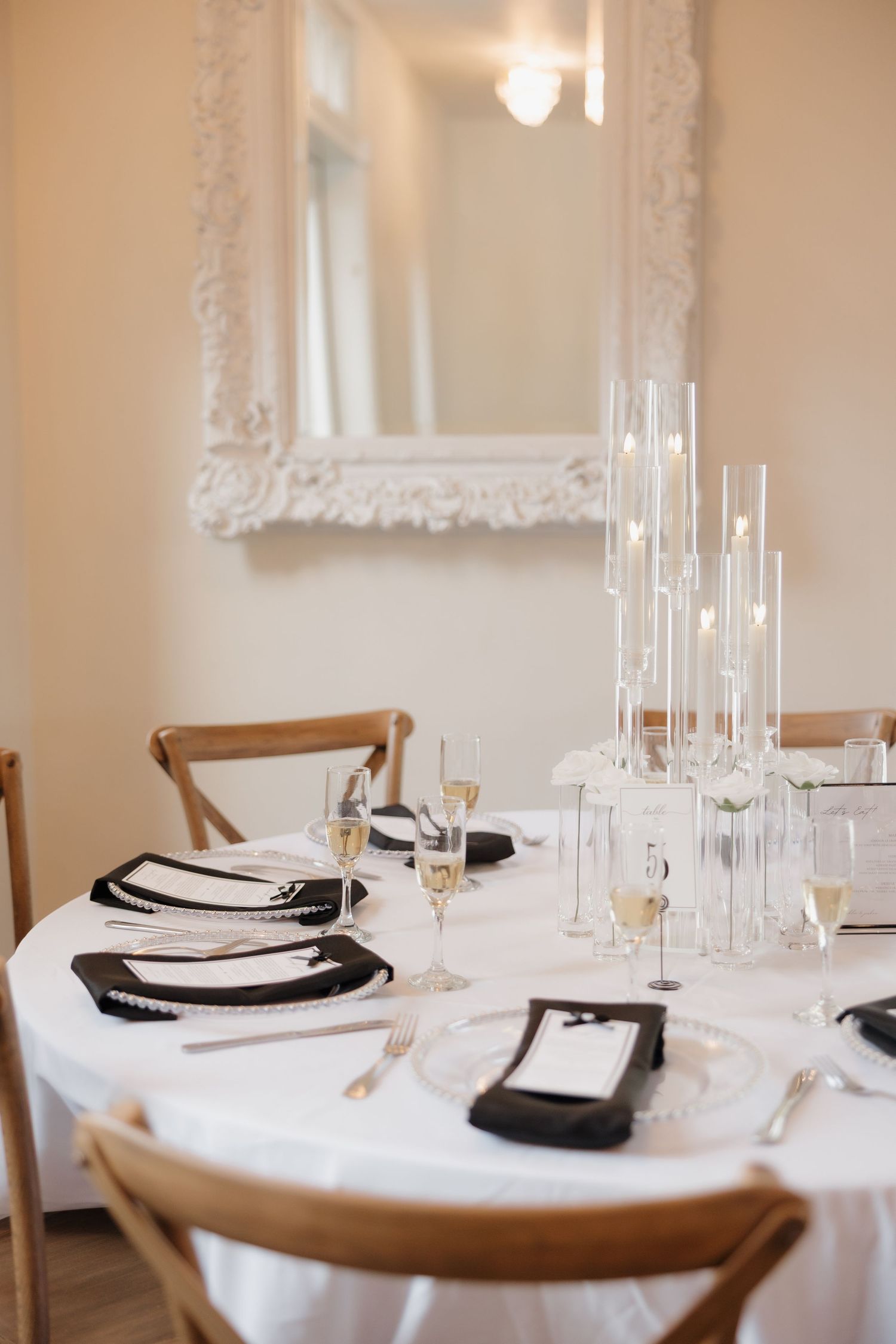 Elegant wedding table setting with white linens, black chargers, and glass candlesticks.
