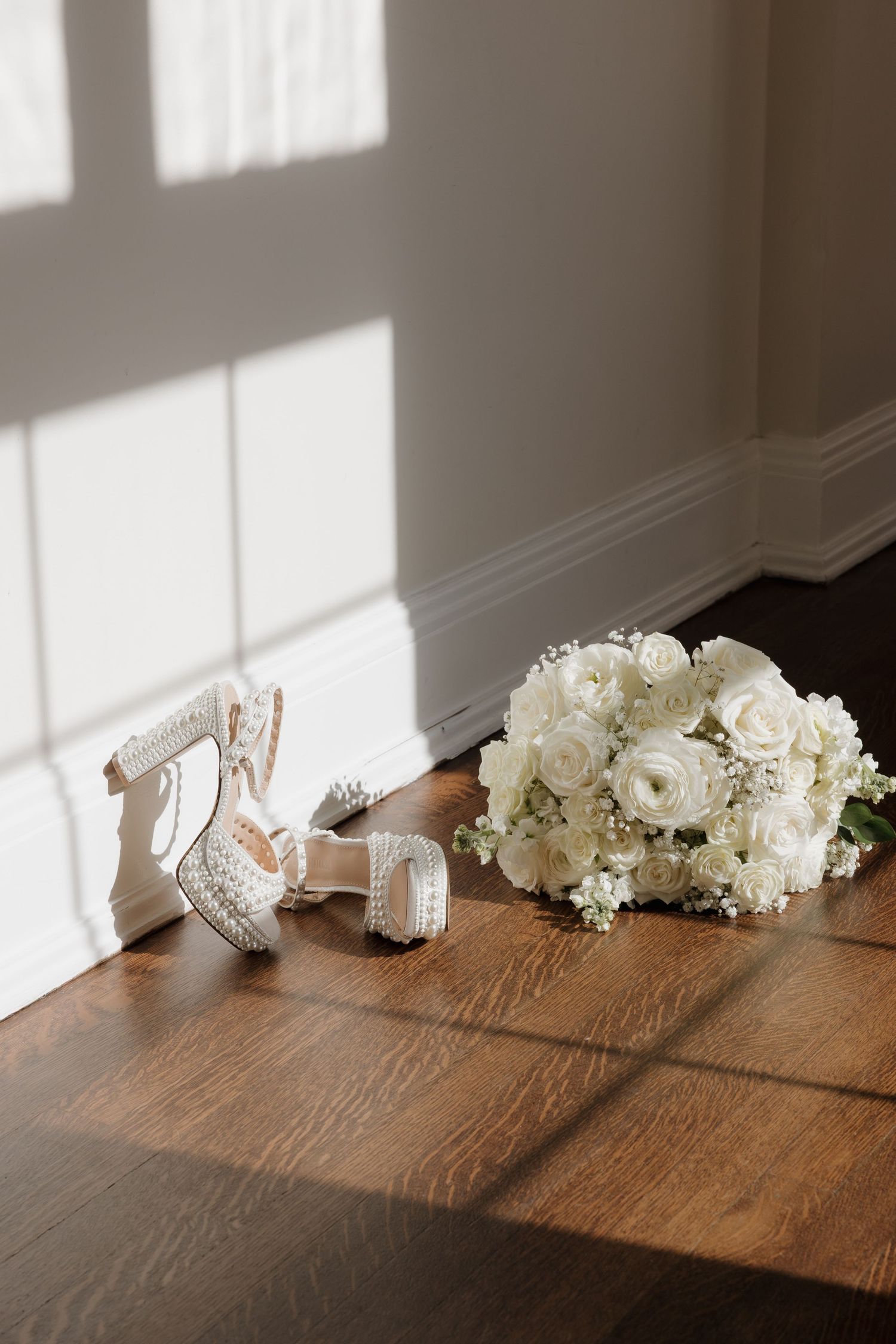 White flowers and bridal accessories create elegant shadows on a rustic wooden table in natural window light.