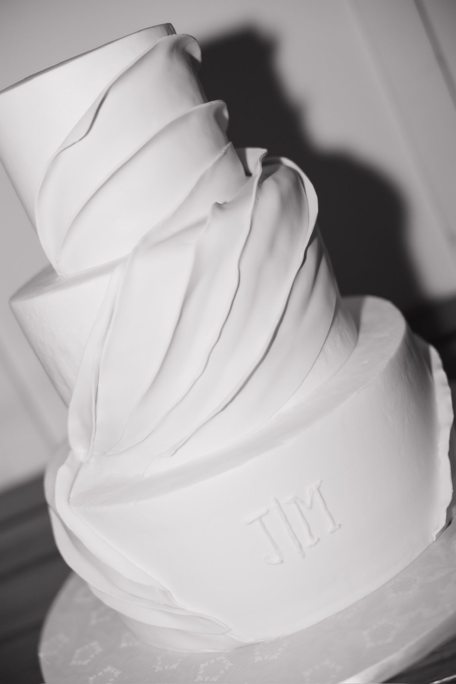 Elegant three-tier white wedding cake with draped fondant design and monogram initials in black and white photography.