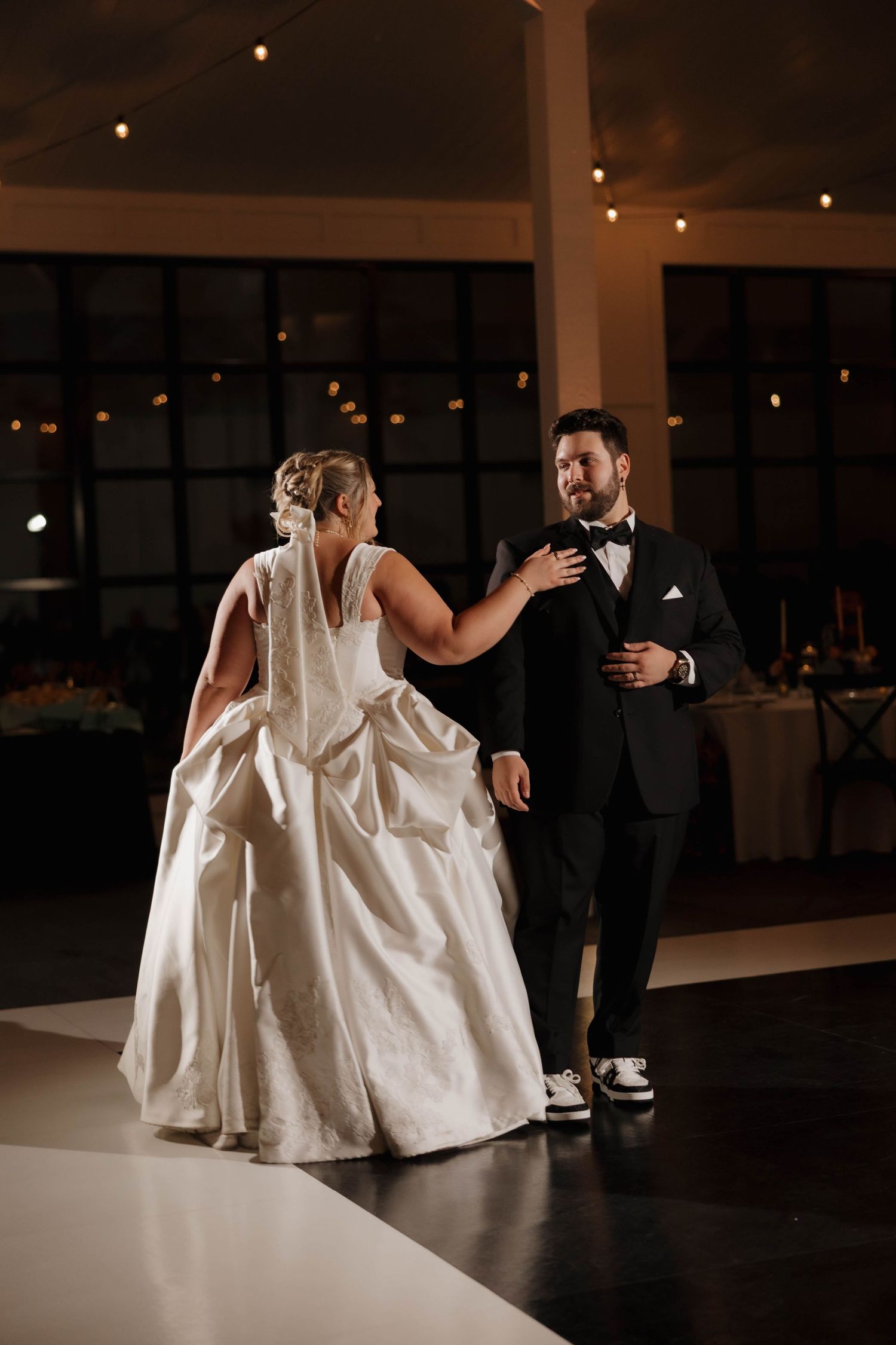 A couple performs a romantic dip during their first dance at a dimly lit wedding reception venue.