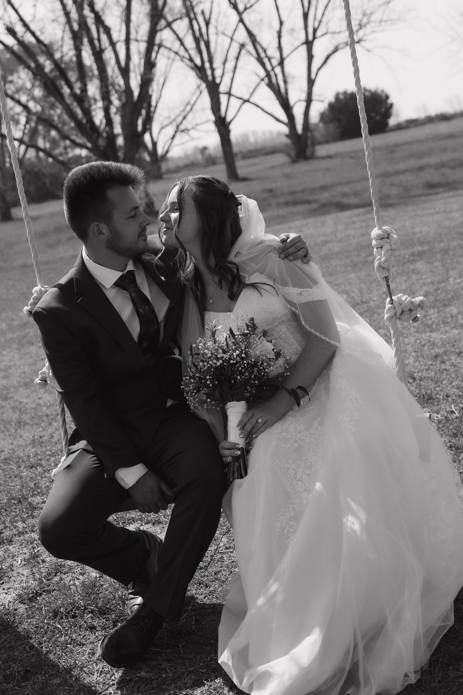 Black and white photo of a bride and groom sharing a romantic moment on a swing, bride holding a bouquet in Pavo, Georgia.