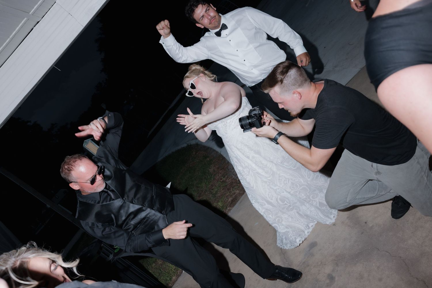 Wedding couple dancing energetically at reception while photographer captures the moment at night.