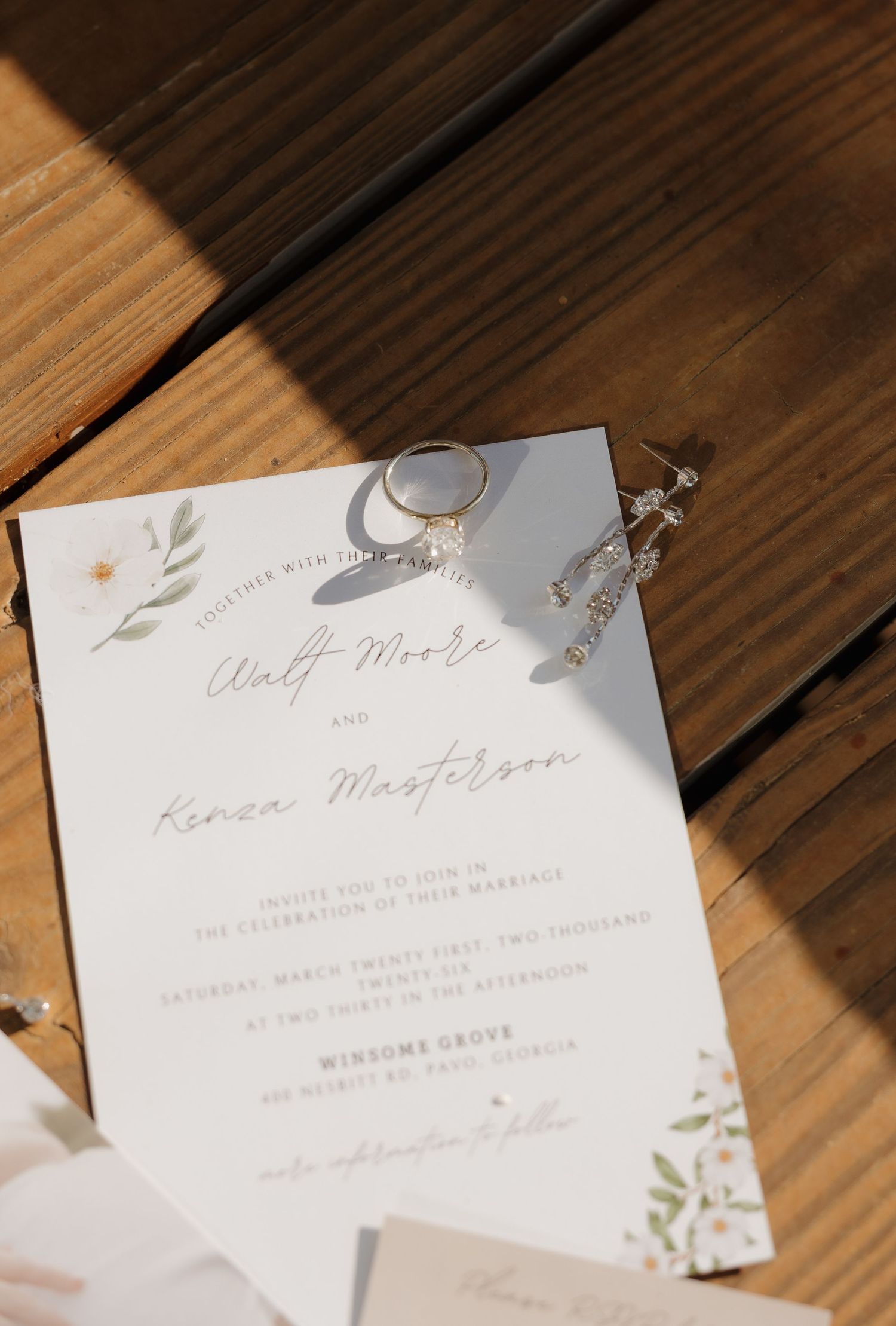 Wedding invitation for bride and groom with floral accents, diamond ring, and crystal earrings on wood, taken by travel wedding photographer