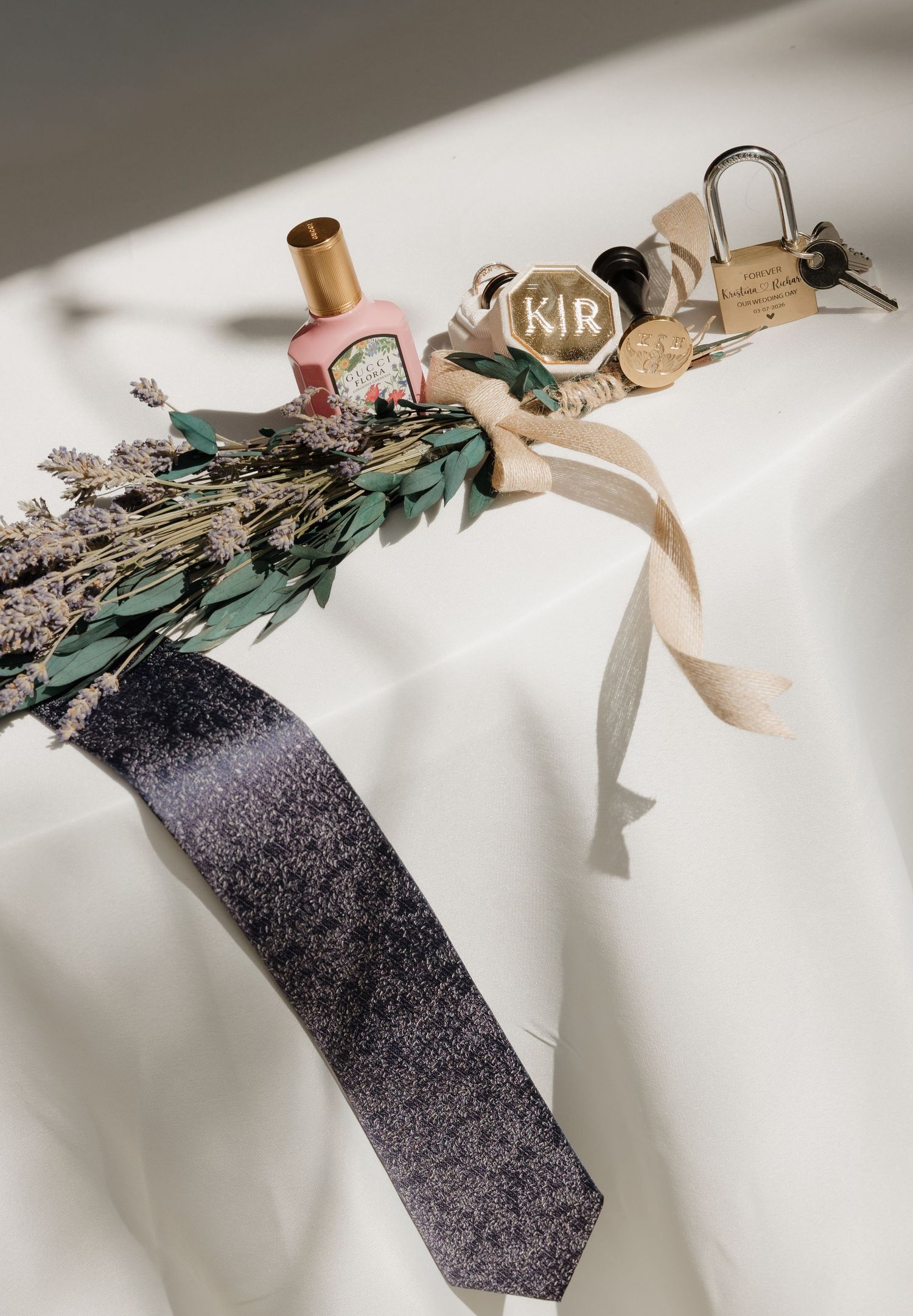A gray necktie arranged with dried flowers, ribbon, and decorative locks on a white surface in soft lighting.