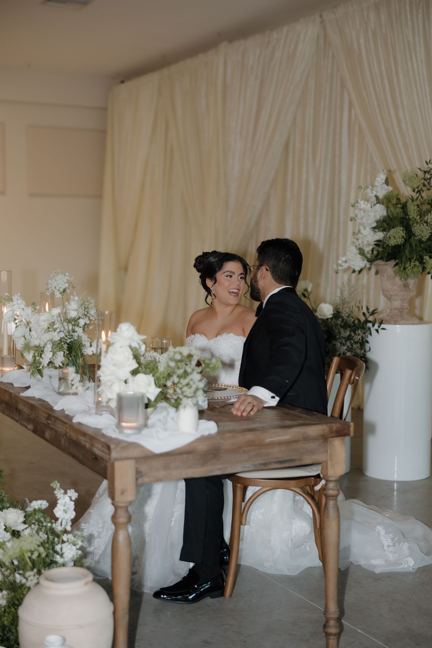 A couple shares an intimate moment at their wedding reception table decorated with white floral arrangements and rustic decor.