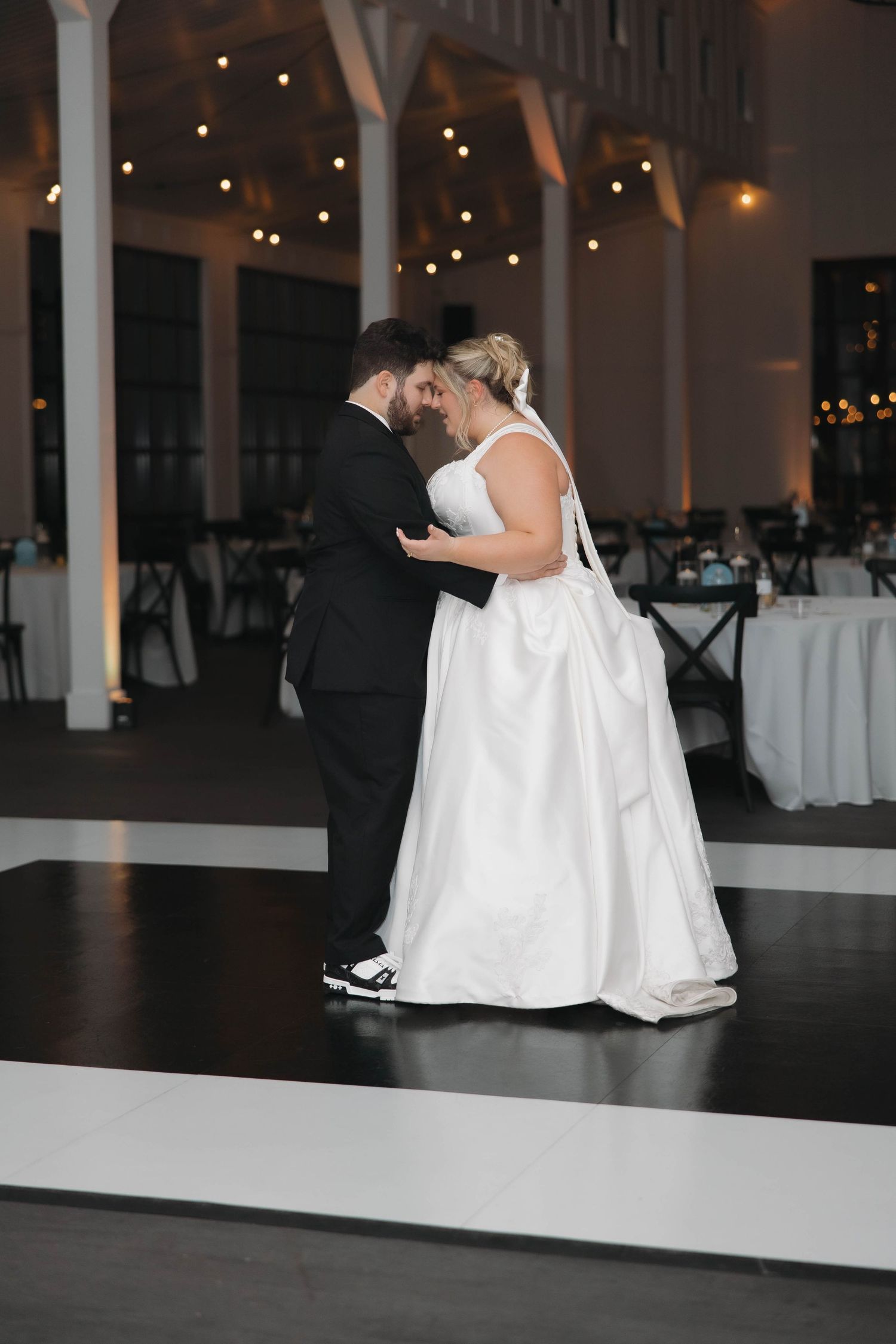Two people in white wedding dresses share an intimate moment on the dance floor at an elegant reception venue.