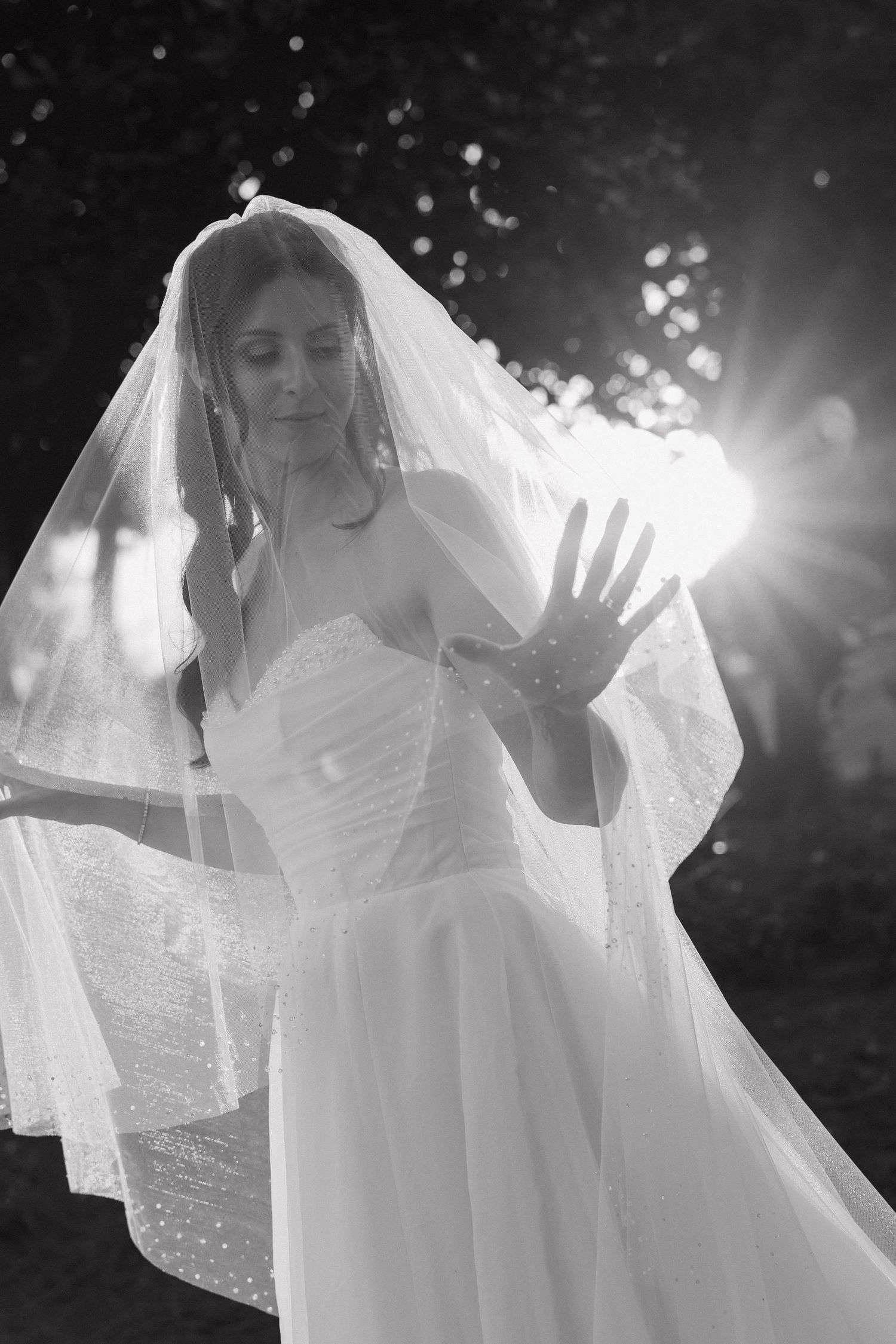 Ethereal black and white photo of a bride in flowing white dress and veil backlit by sunlight.