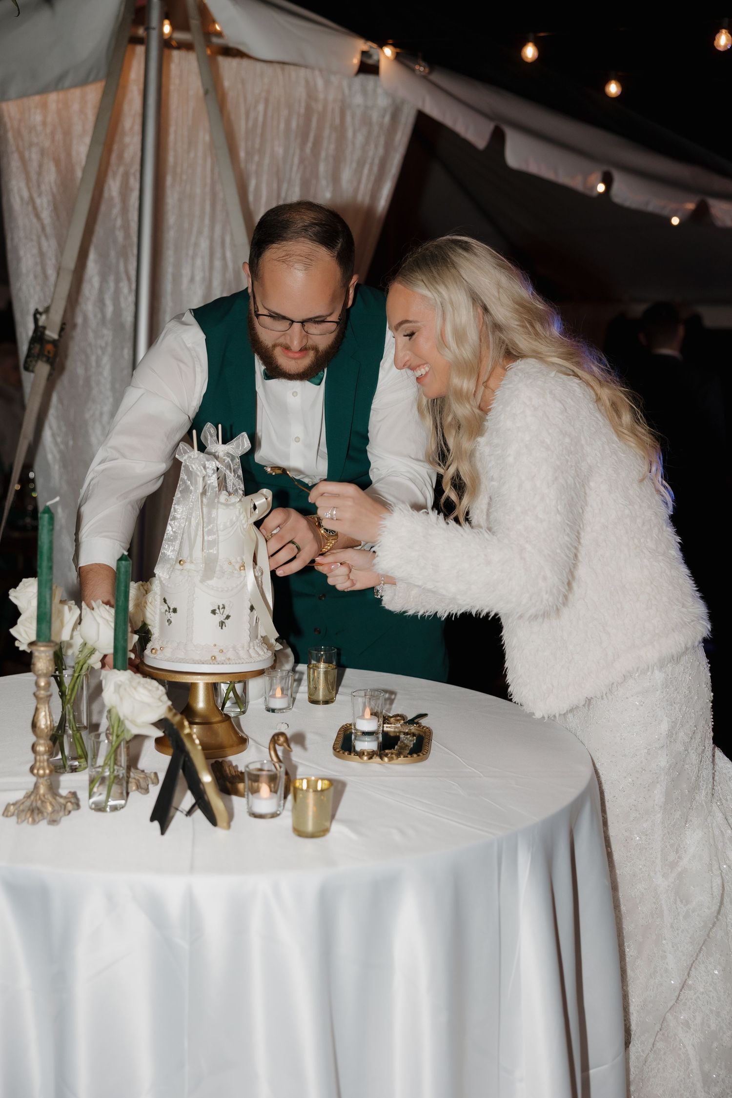 A couple in wedding attire shares an intimate moment while cutting their white wedding cake at an elegant reception.