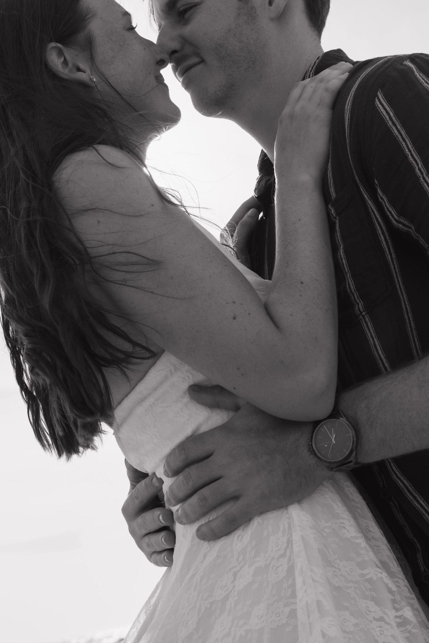 Black and white photo of a romantic couple embracing and about to kiss, man wearing a watch.