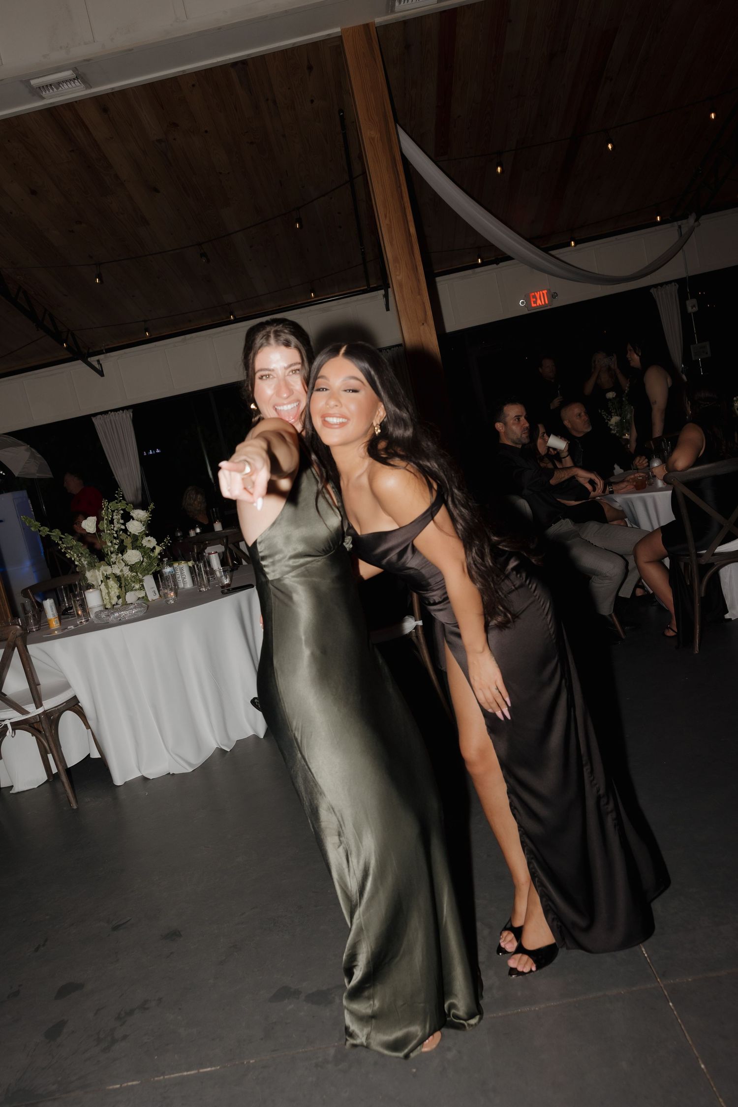 Two women in elegant evening gowns, one in olive silk and one in black, pose together at a formal event.