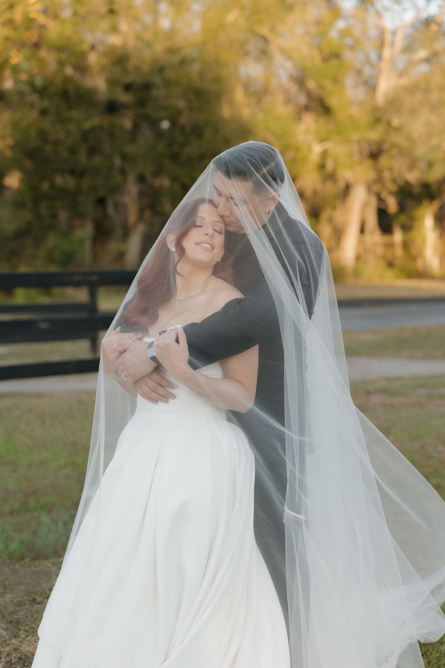 A romantic wedding couple dances together outdoors during golden hour while the bride's veil flows in the autumn breeze.