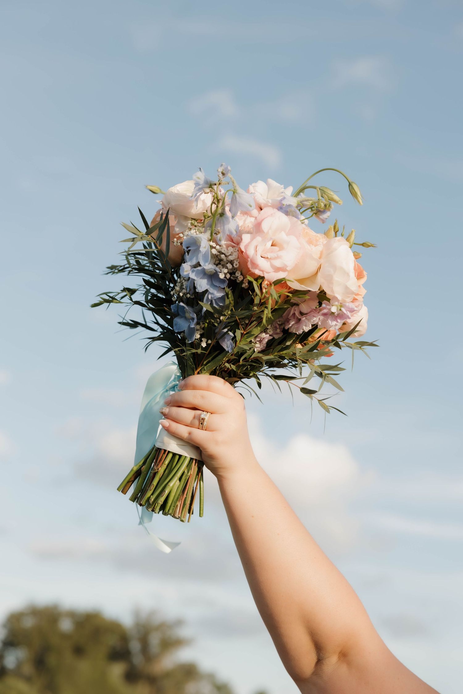 Hands raised against a blue sky hold a beautiful bouquet of pink roses and greenery in a sequence of four photos.