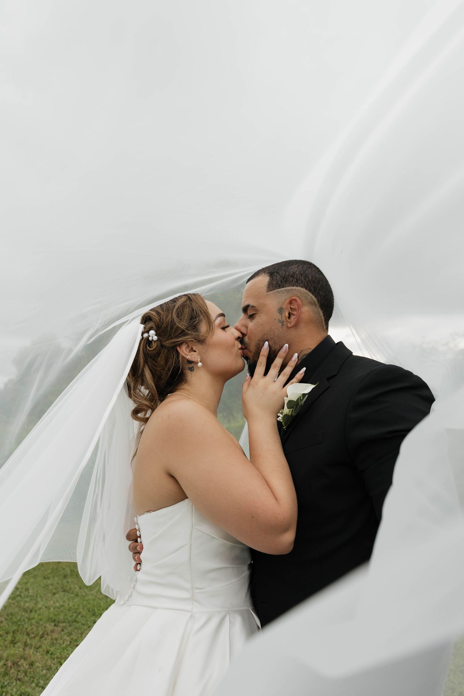 Bride and groom share a romantic kiss under a flowing white veil on their wedding day.