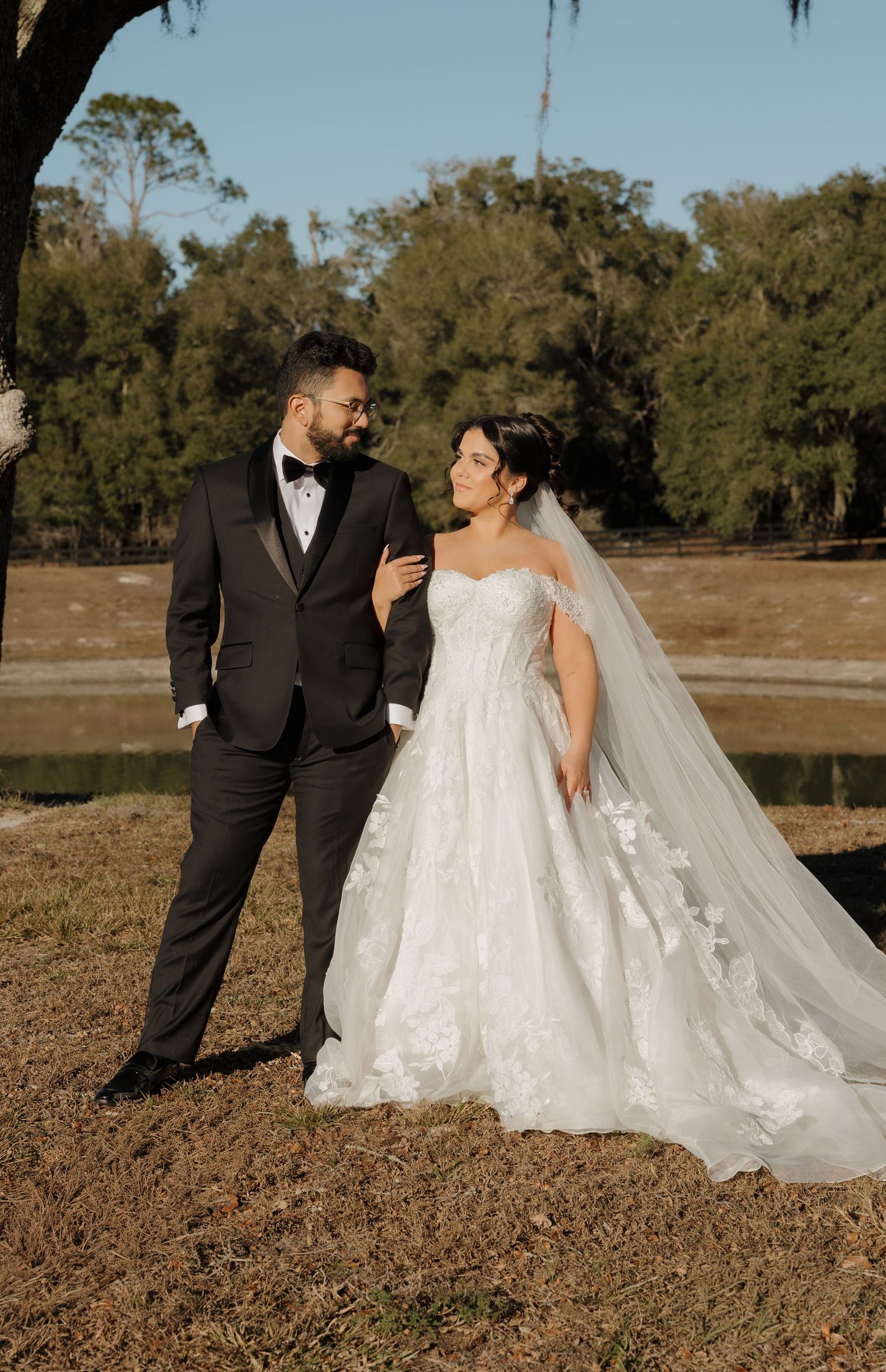 Newlywed couple shares romantic moments during outdoor wedding photoshoot by a lake on autumn day.