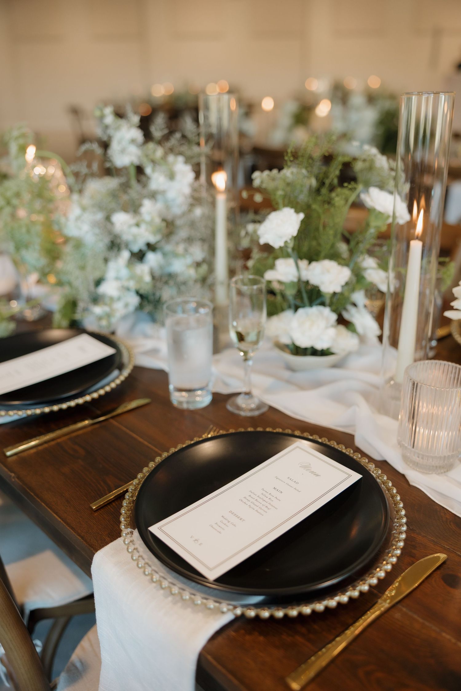 Elegant wedding table settings with black charger plates, white menus, and floral centerpieces on dark wooden tables.