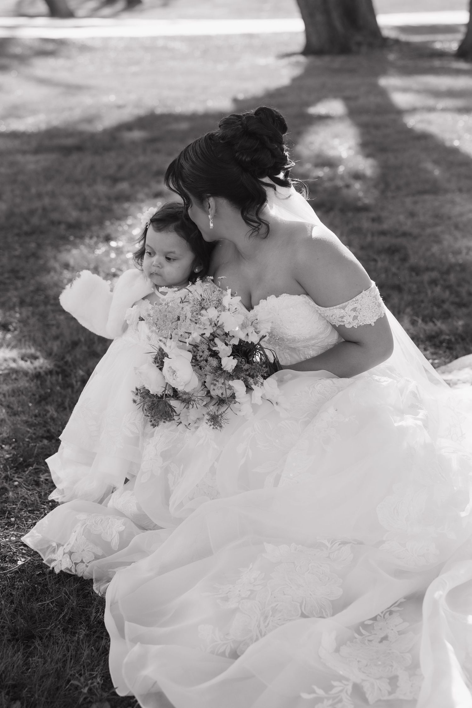 A bride in a flowing white wedding dress sits gracefully on grass in a black and white photograph.